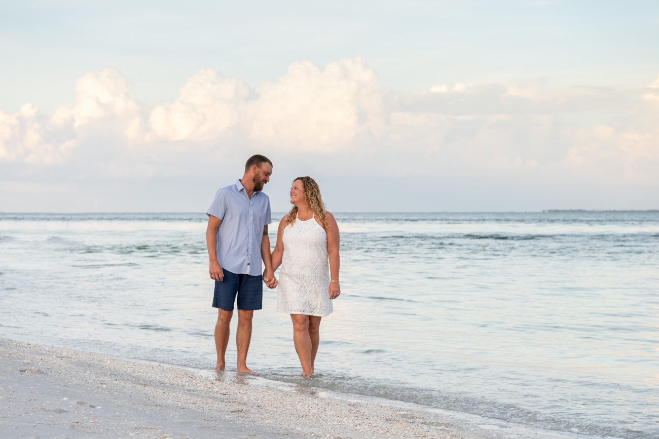 engaged couple walk along beach holding hands