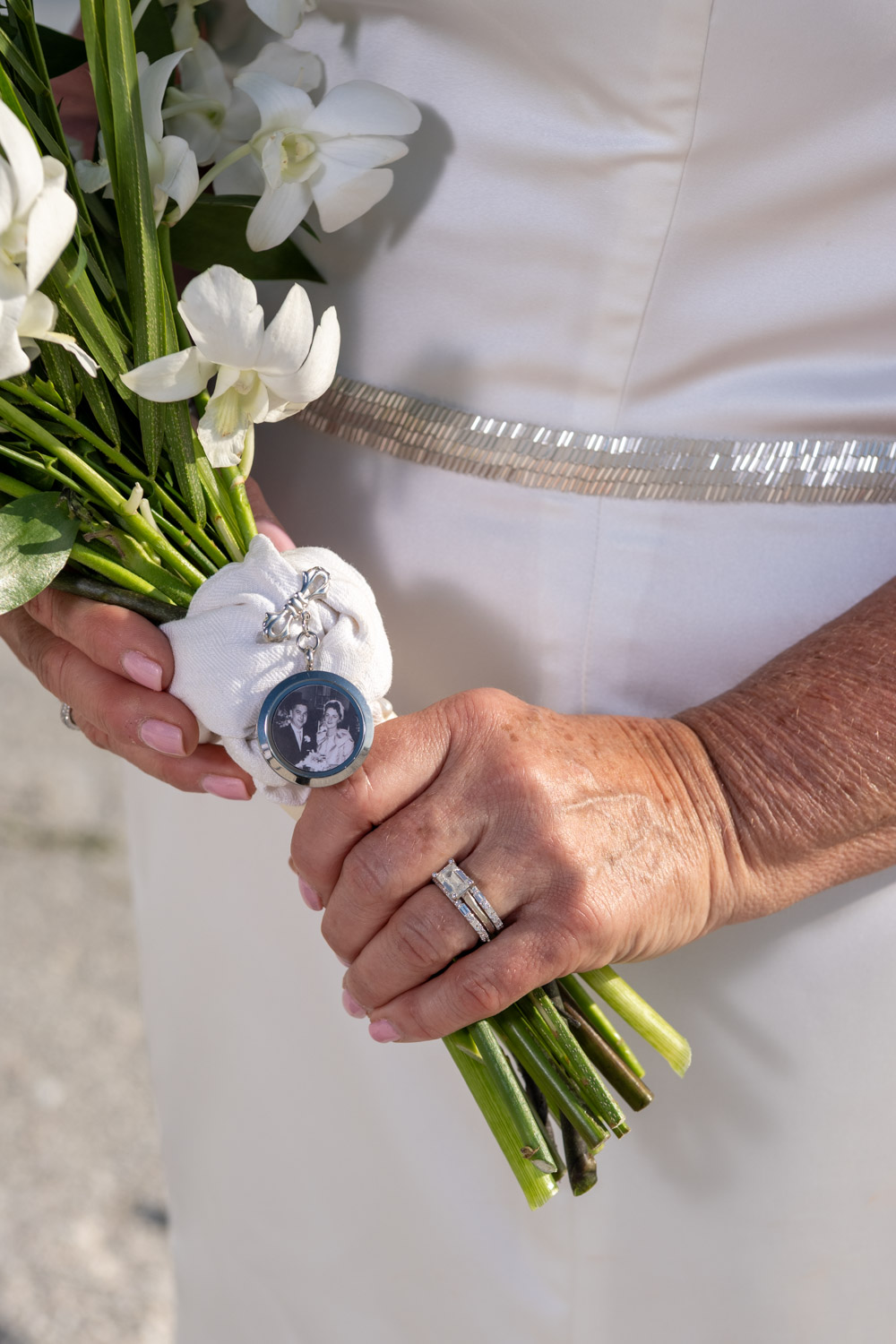 bride shows off her wedding ring and locket with a photo of her parents who passed away that is attached to her bridal bouquet
