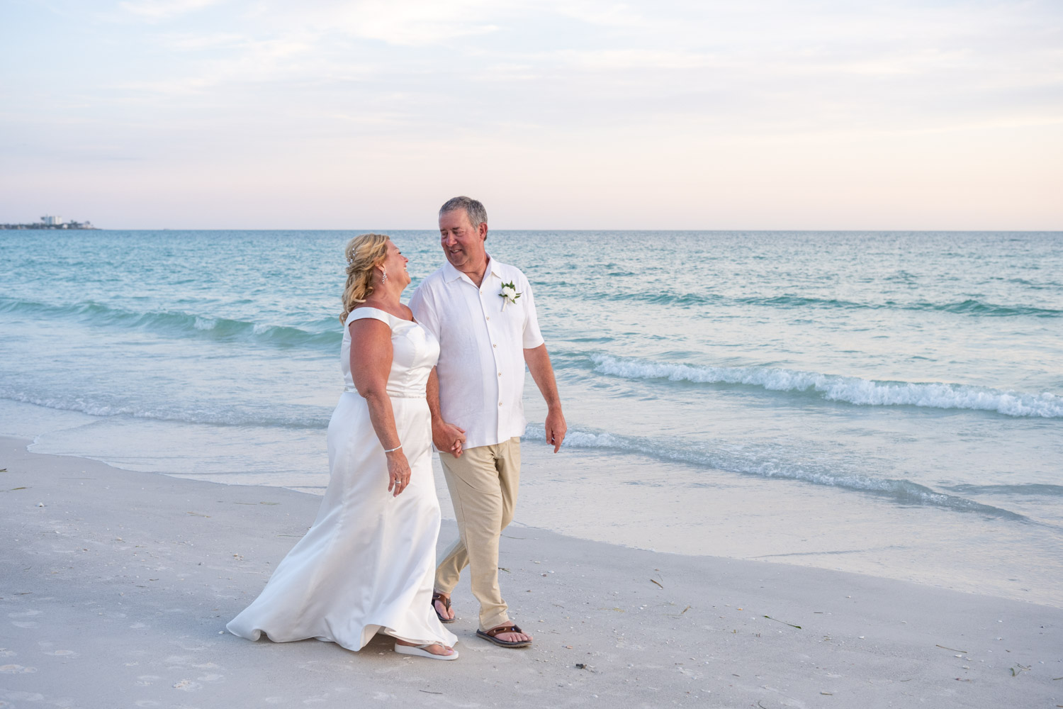 bride and groom walk along the beach as the sky turns a soft pink