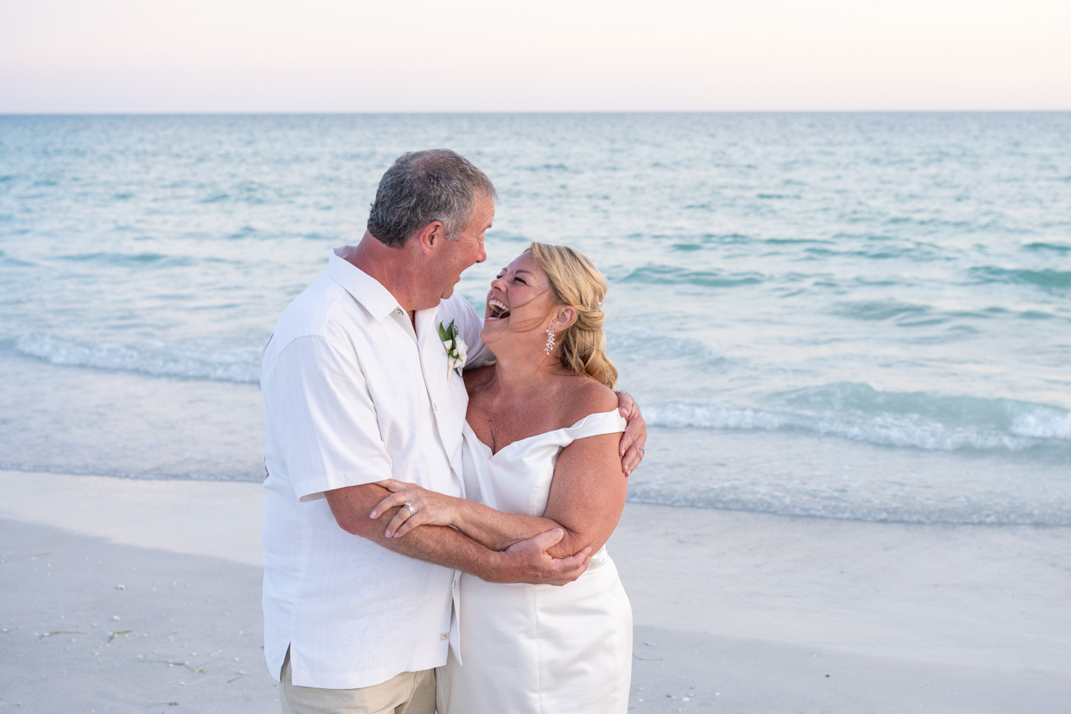 bride laughs as her husband holds her as the walk along the beach