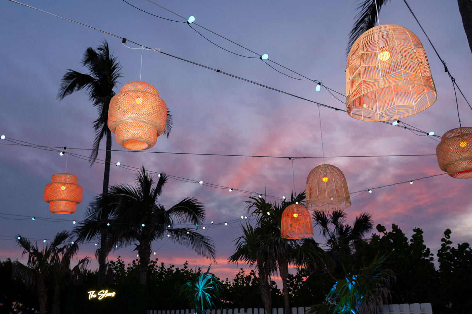 lanterns softly glow against a purple sky, hung between palm trees at wedding reception at Lido Beach Resort