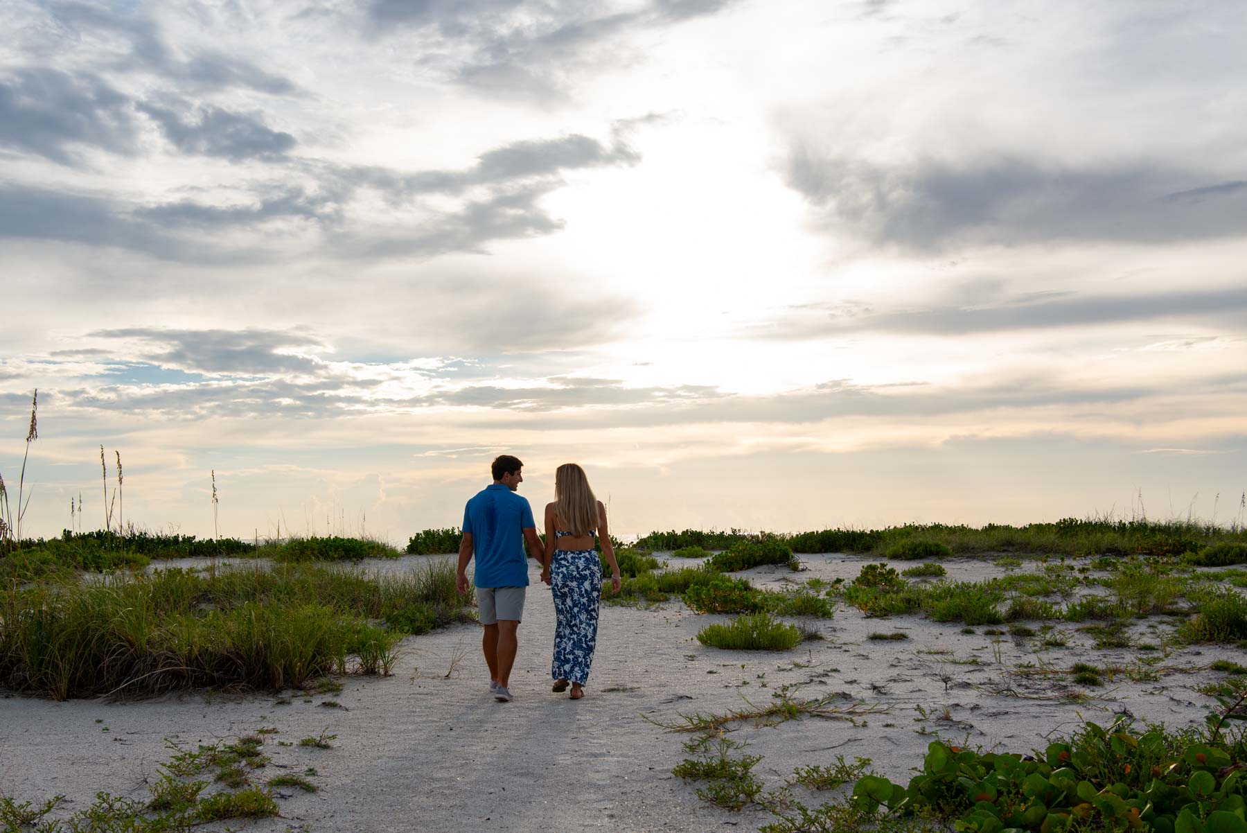 newly engaged couple walk along path to Boca Grande Beach