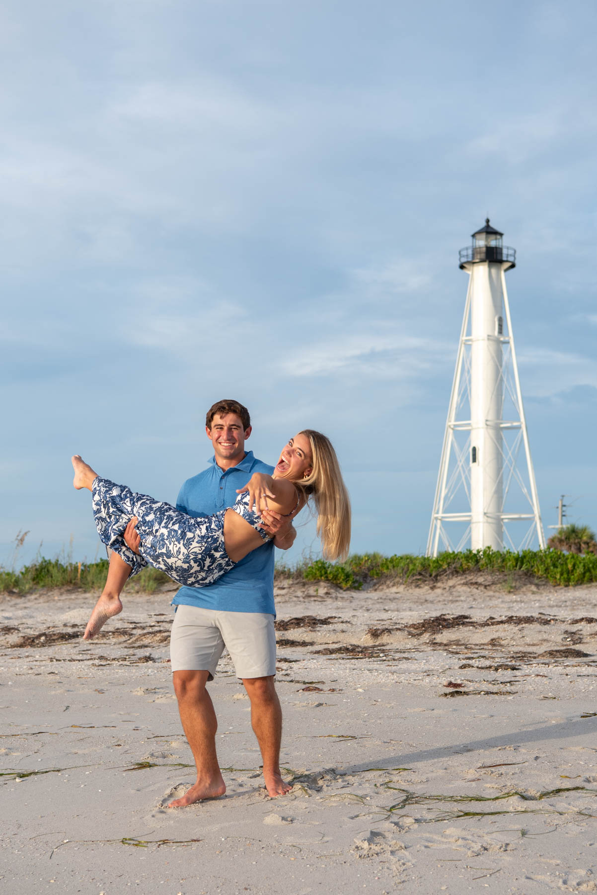 Will lifts Hannah up and twirls her as she shows off her ring with the Boca Grande lighthouse in the background