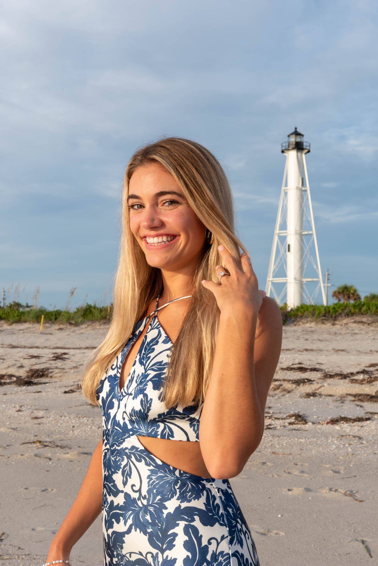 Hannah shows off her engagement ring as she pulls her hair back as the sun glows on her face with the Boca Grande lighthouse in the background