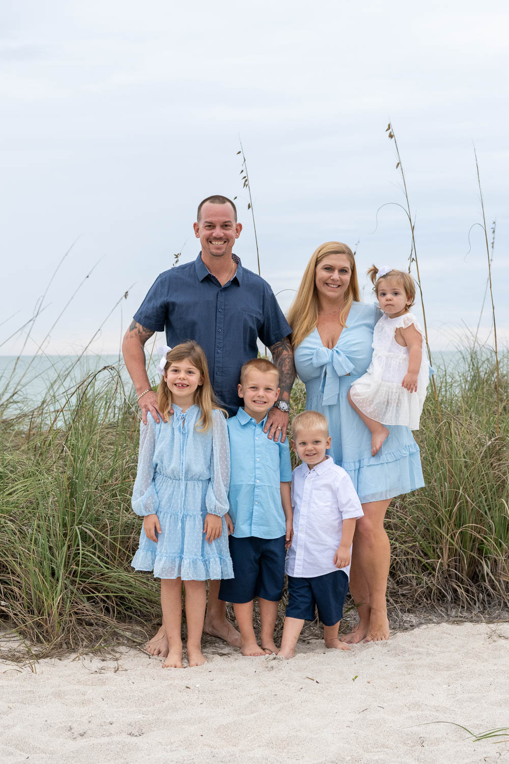 parents with their four children, all dressed in blue, on the beach for a family photo session