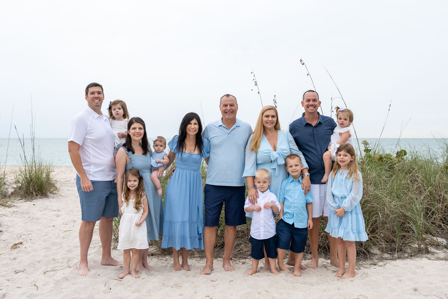 large family all dressed in blue standing with seagrass behind them and the beach