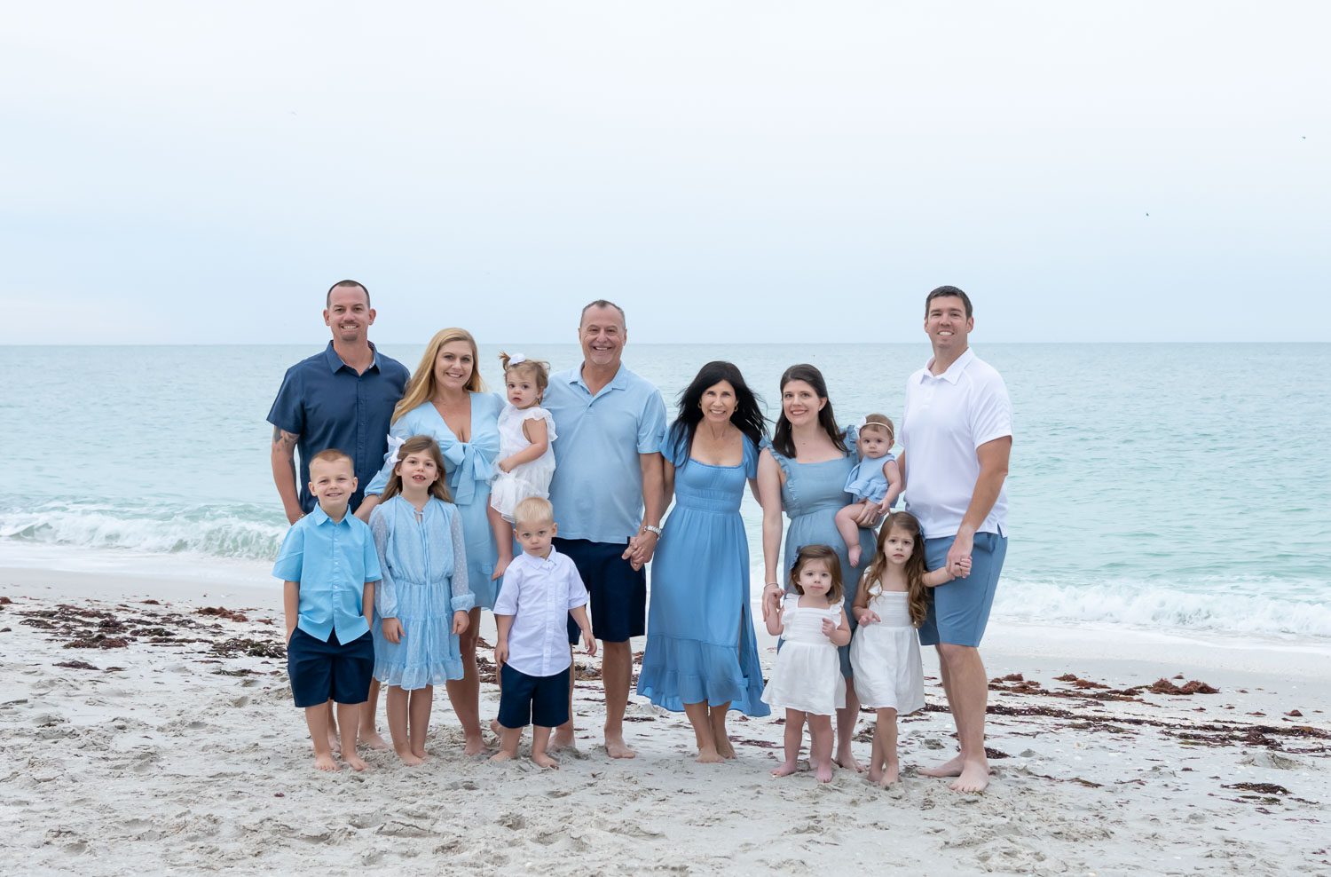 large family stands together on a beach