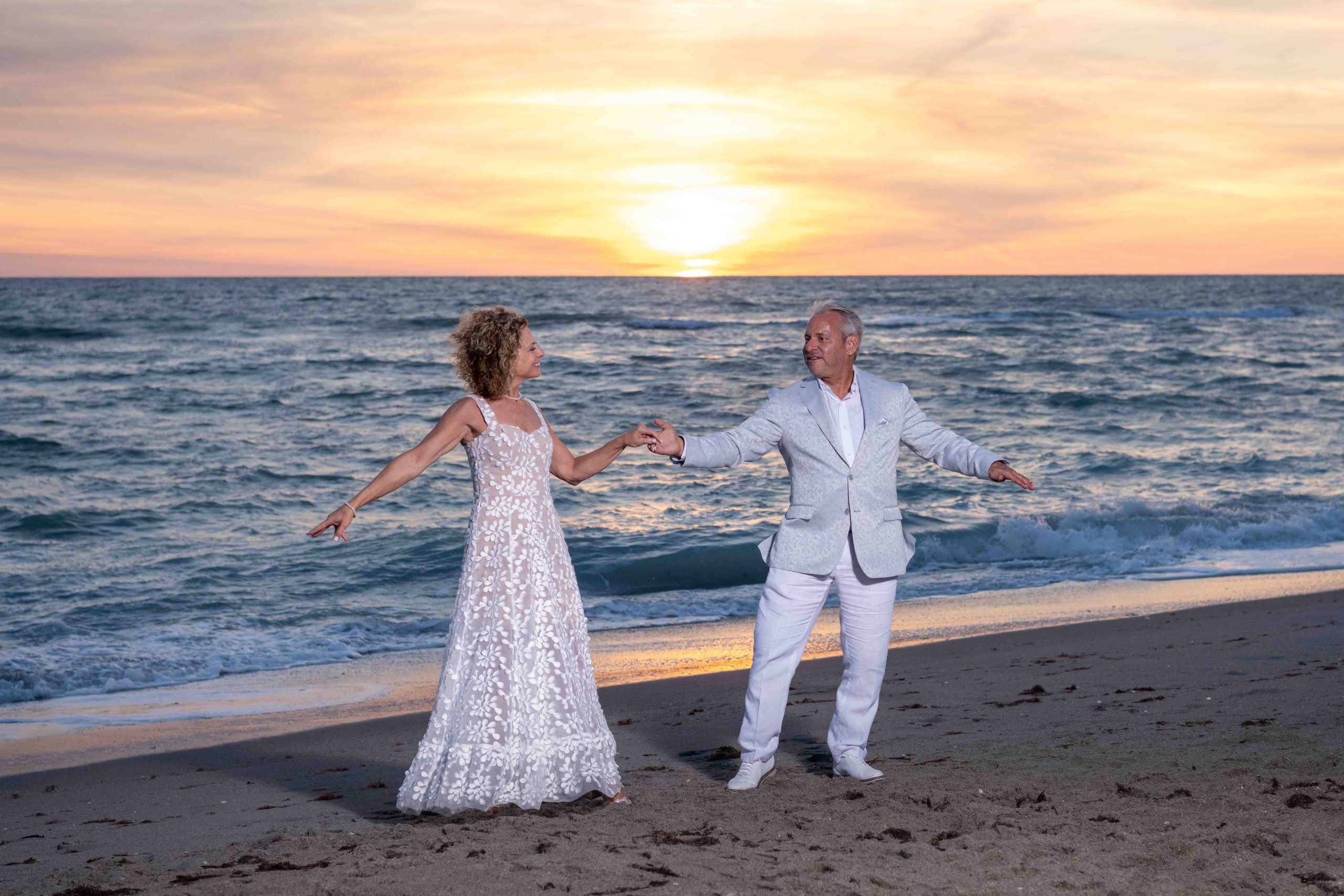 bride and groom show off their dance moves on the beach at sunset