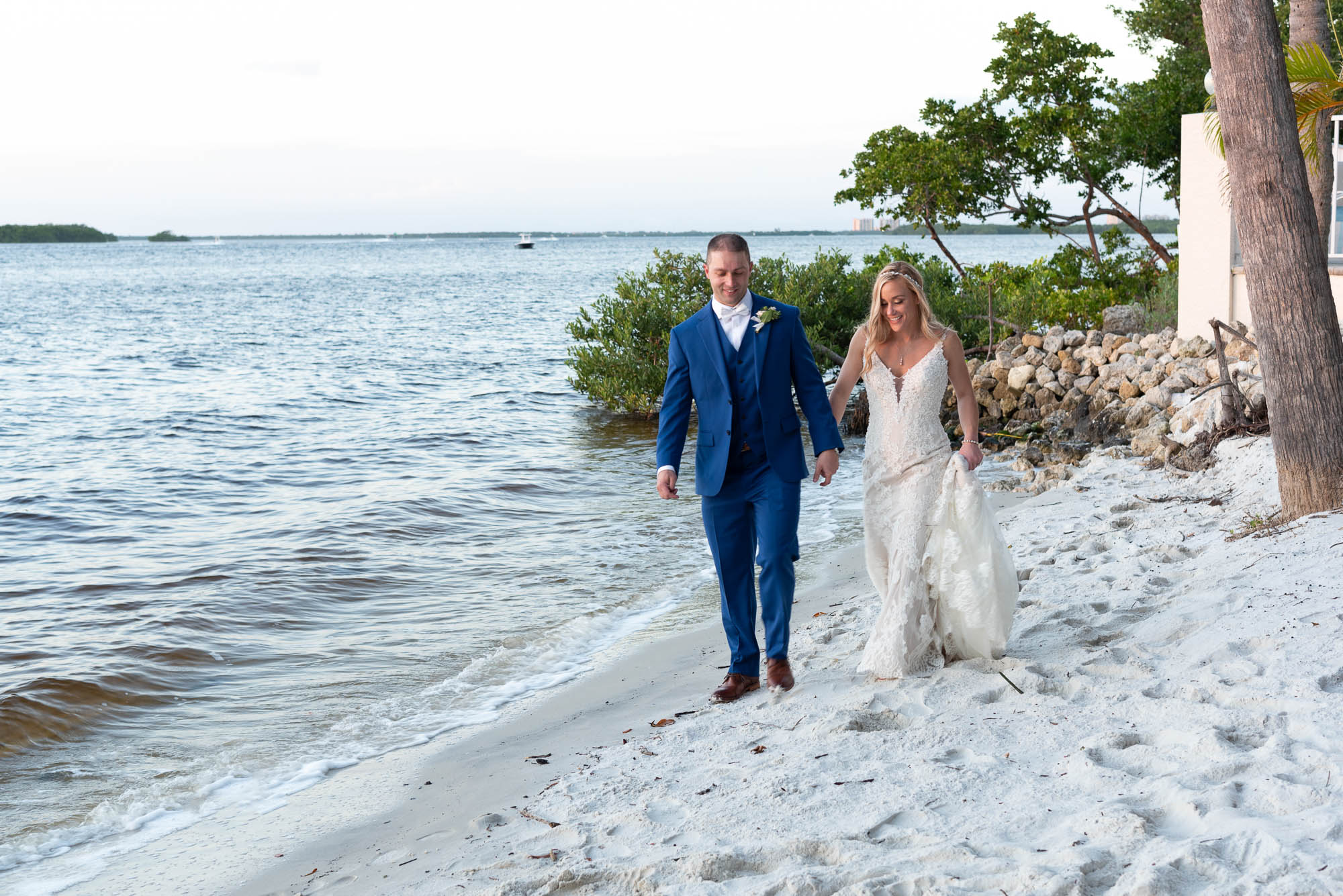 bride and groom hold hands as they walk along the waterfront