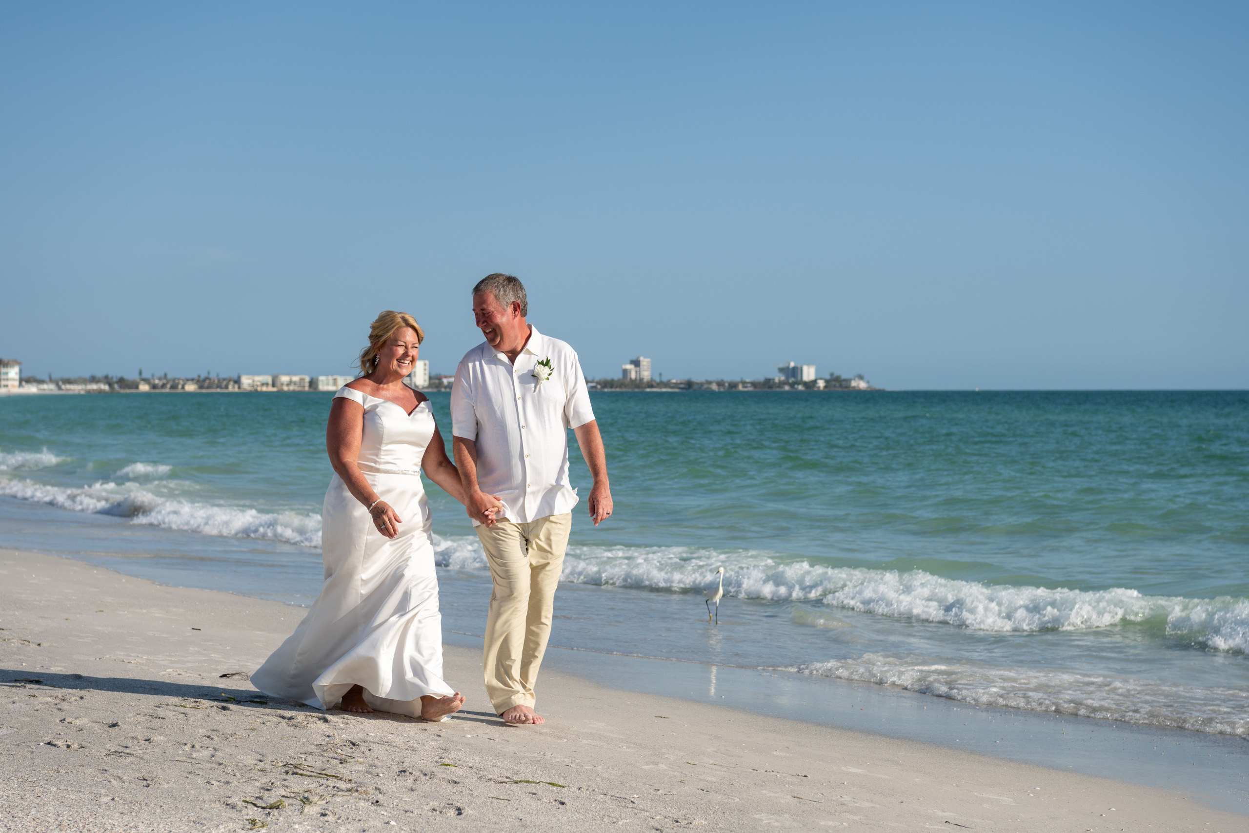 bride and groom hold hands as they walk along the beach
