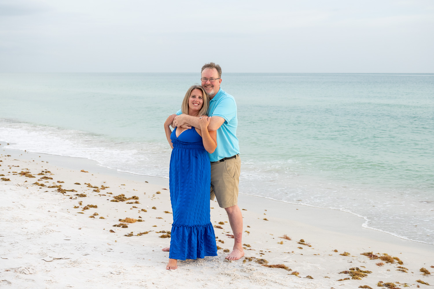 Lido Beach family session with husband wrapping his arms around his wife while standing on Lido Key Beach