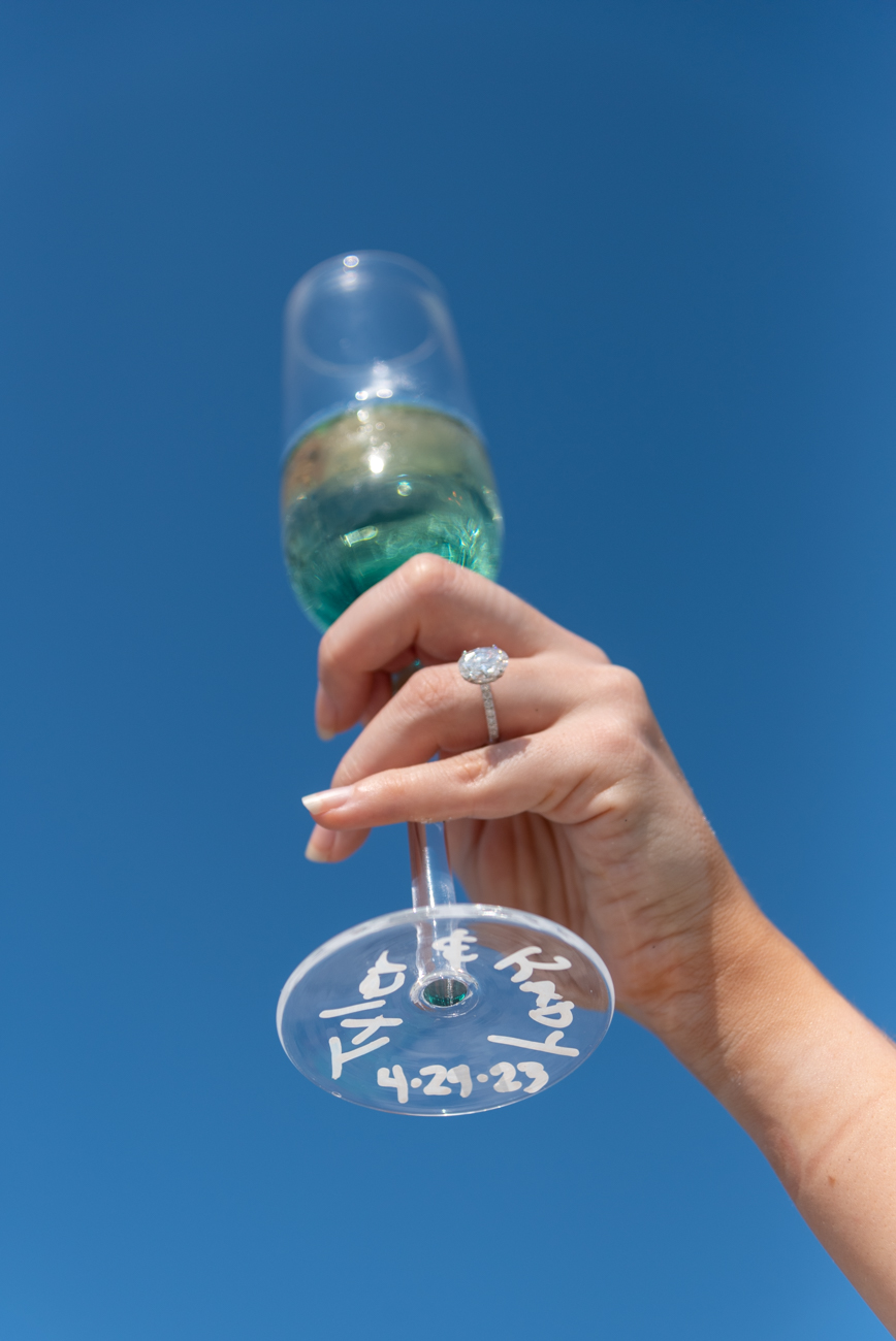 girl holds up a champagne glass to show off her new ring and the glass has their names on it