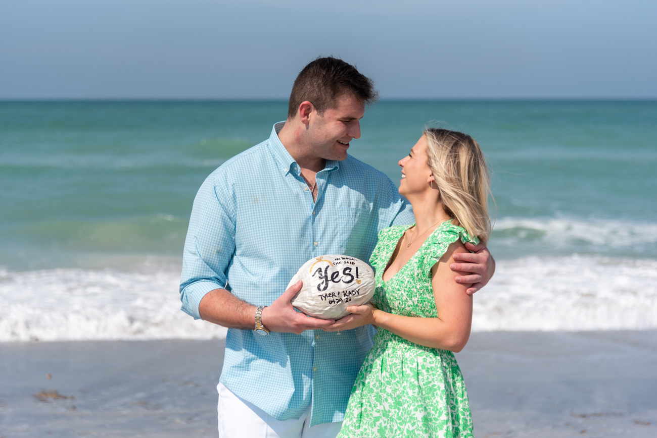 after surprise proposal on Palm Island, couple hold up a painted coconut and smile at each other