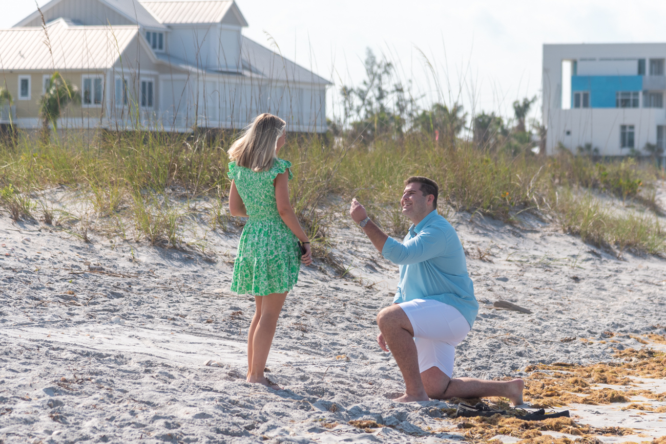man drops down to his knee on the beach to propose to his girlfriend