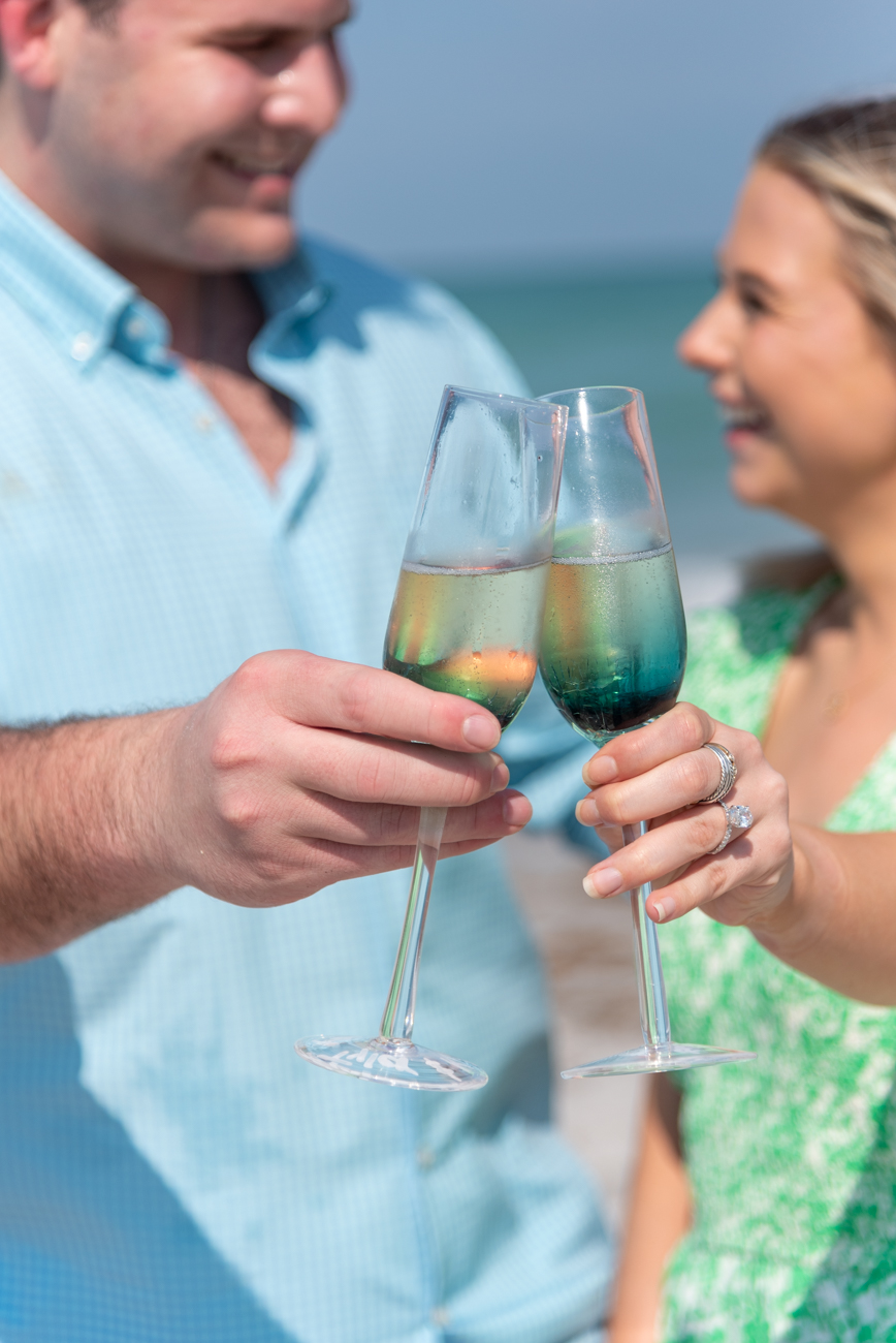 couple hold their champagne glasses out as they smile at each other in the background