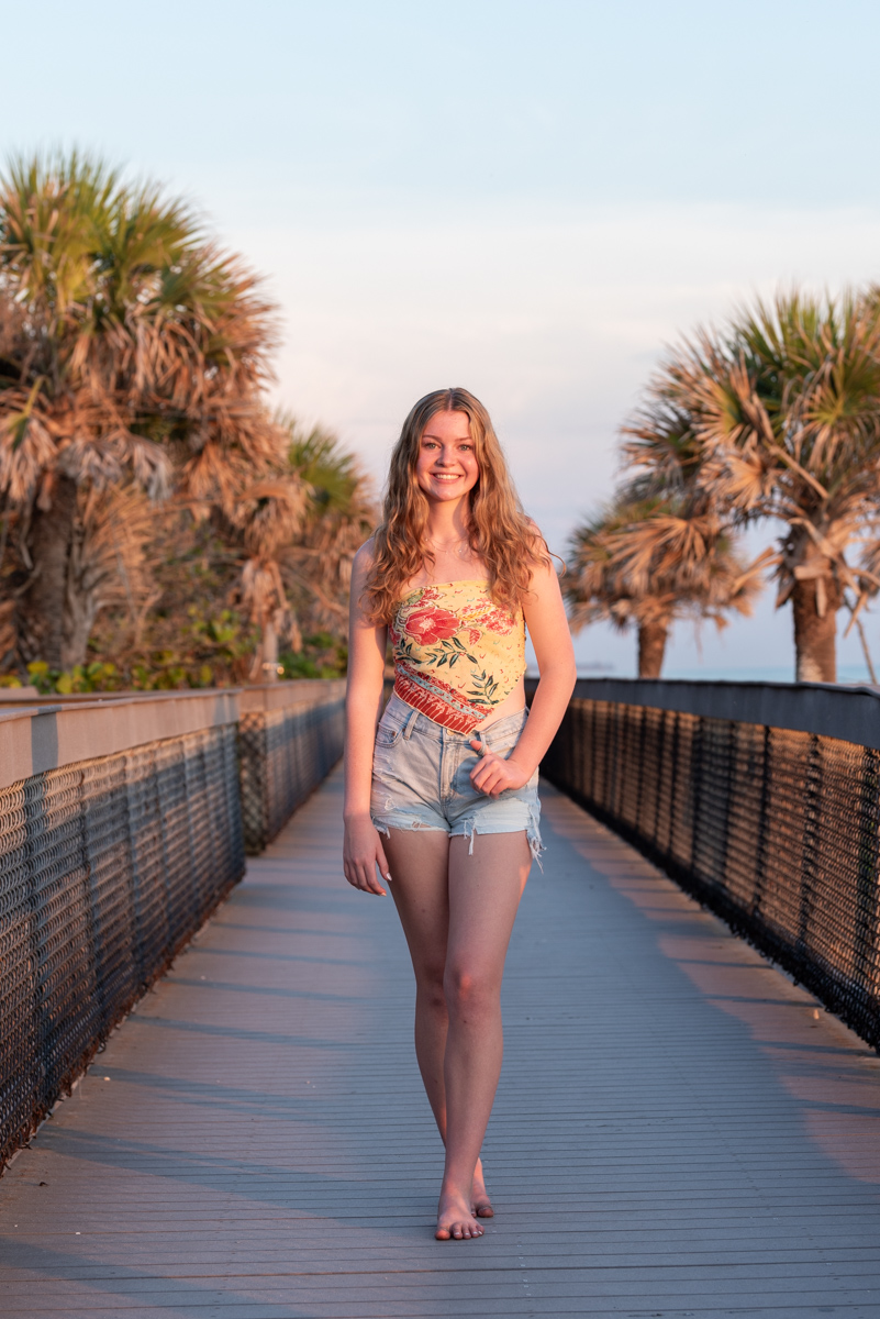 senior photo of girl dressed in flower top and cut off jeans on boardwalk on Caspersen Beach