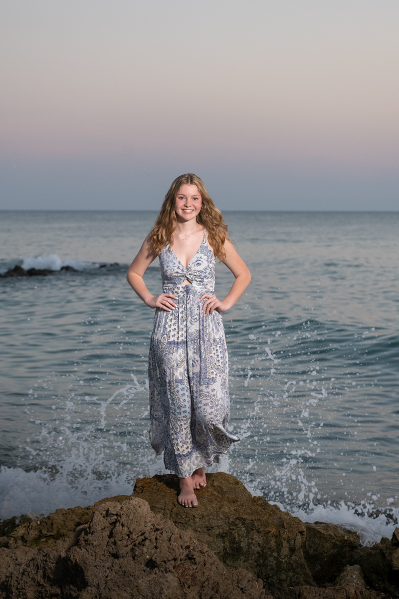 senior girl stands on rock at Caspersen Beach as a wave splashes behind her