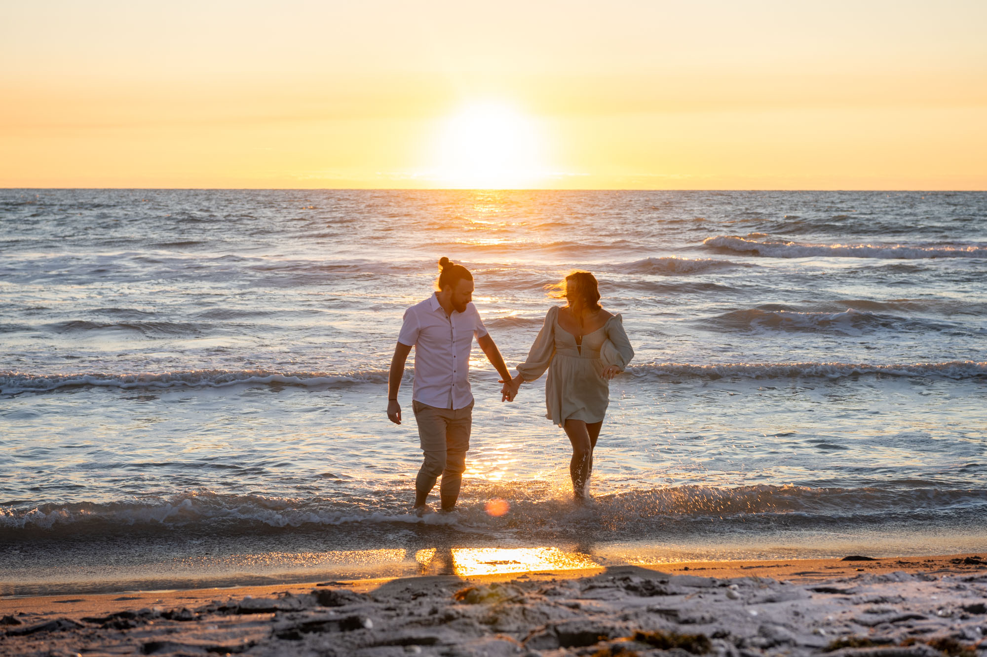 guy and girl splash in the Gulf at Englewood Beach while holding hands as the sun starts to set