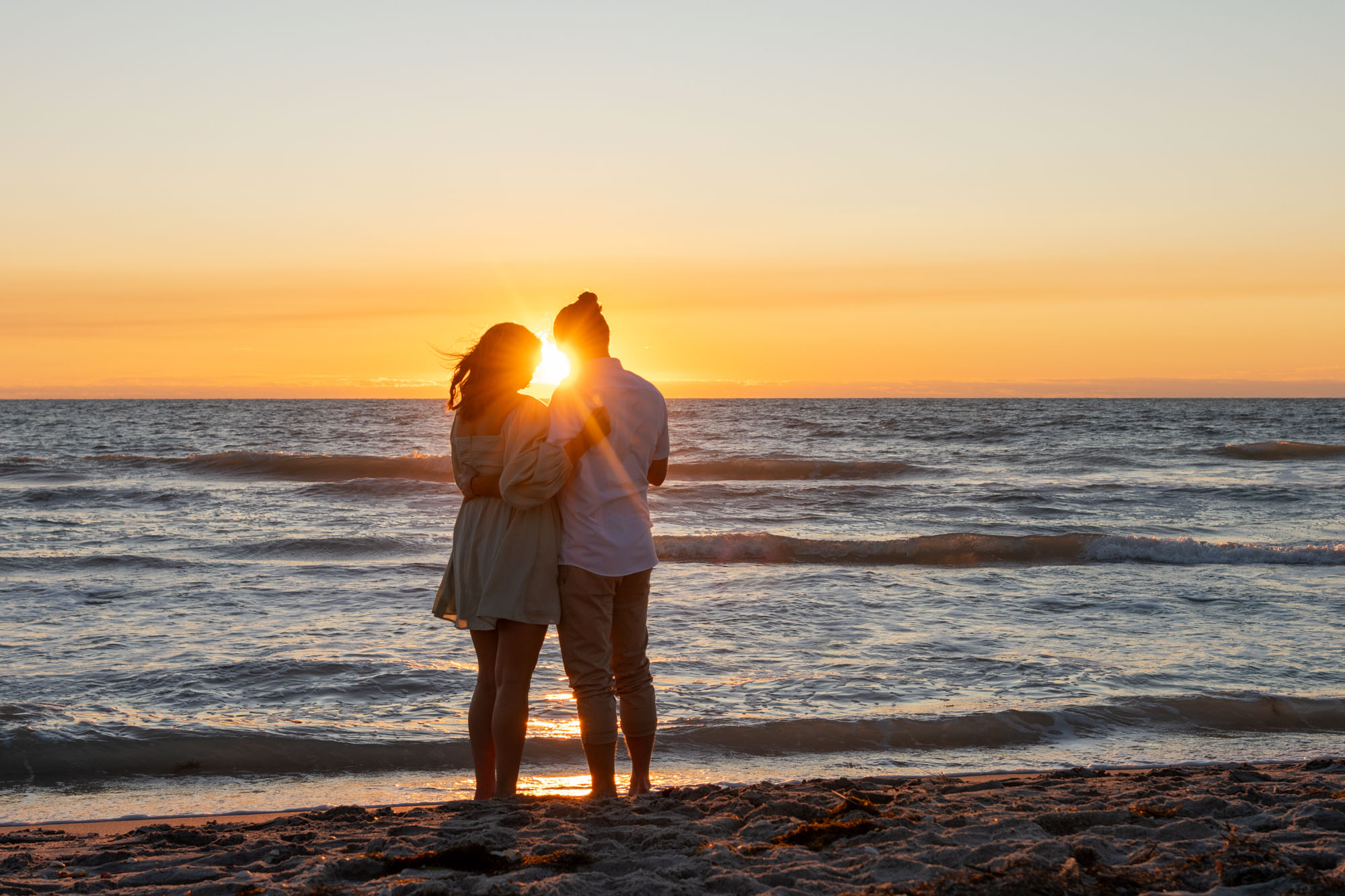 newly engaged couple watch the sunset as it shines between their heads