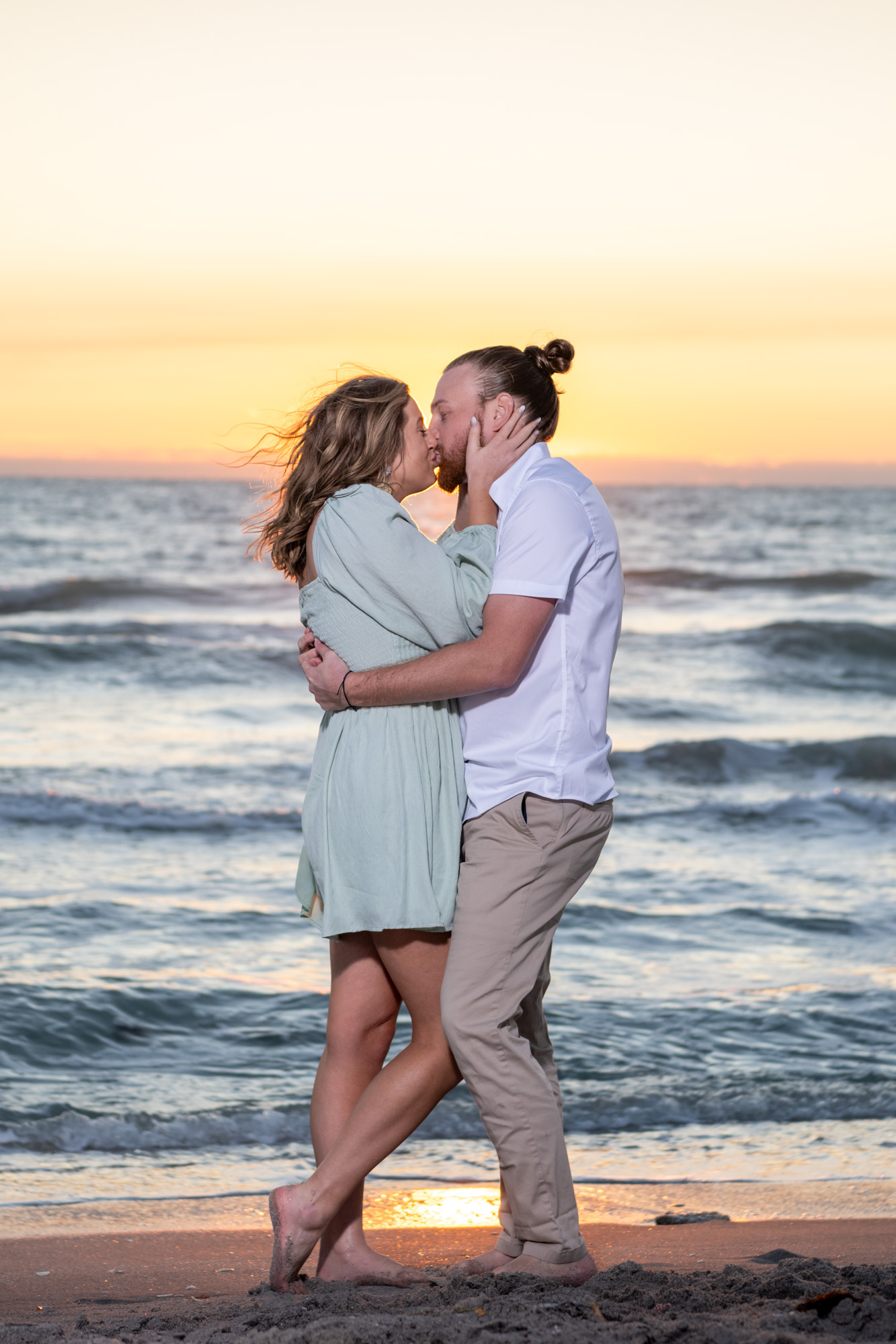 couple kiss as the sky shines a beautiful orange glow from the sunset