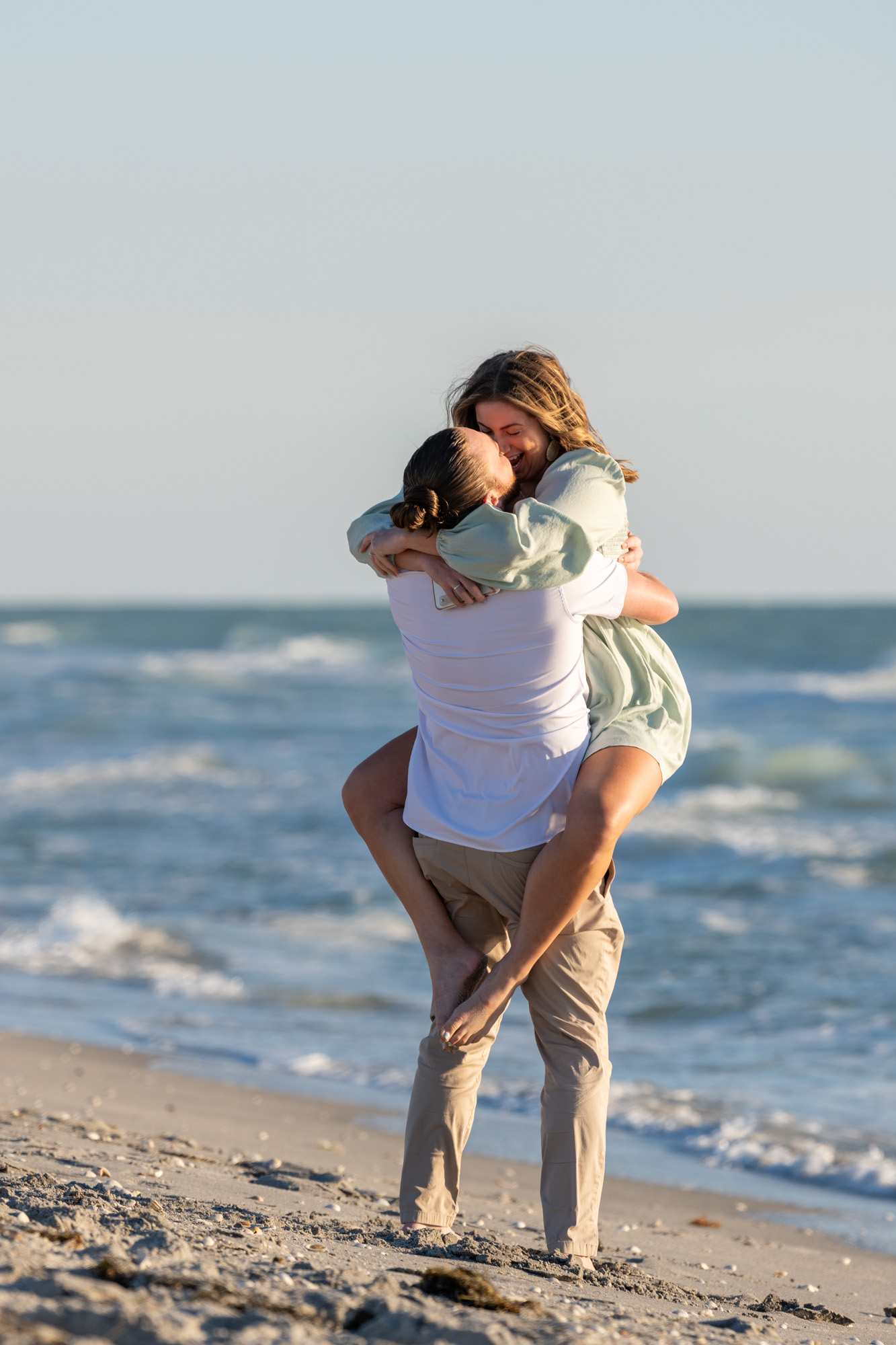 girl excitedly says yes and jumps up on him wrapping her legs around him after an Englewood Beach engagement