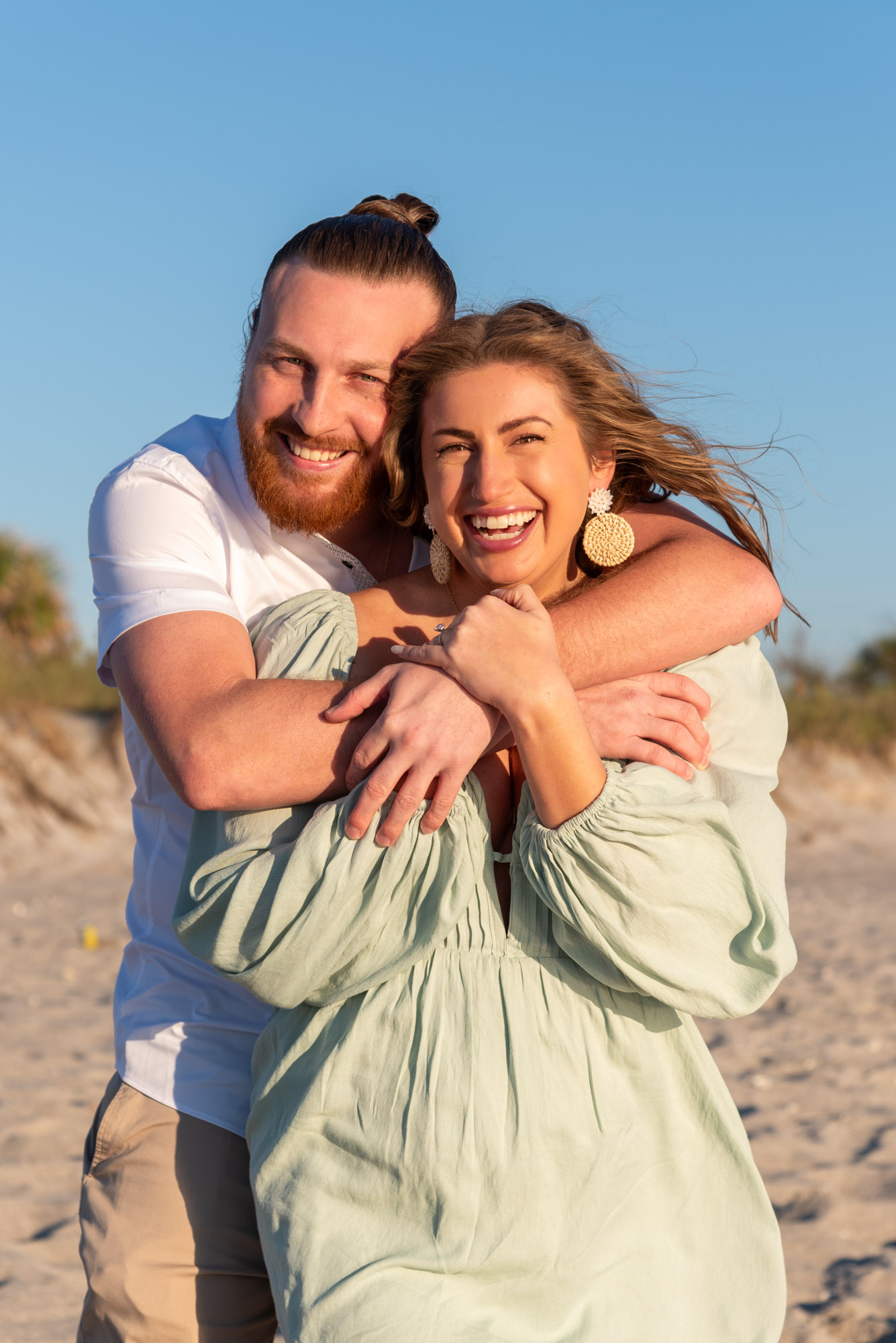 man wraps his arms around his new fiance as they both smile brightly