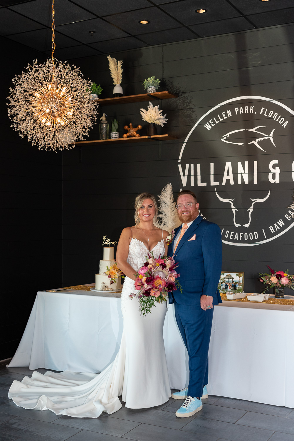 bride and groom pose in front of cake and table before wedding reception at Villani & Co