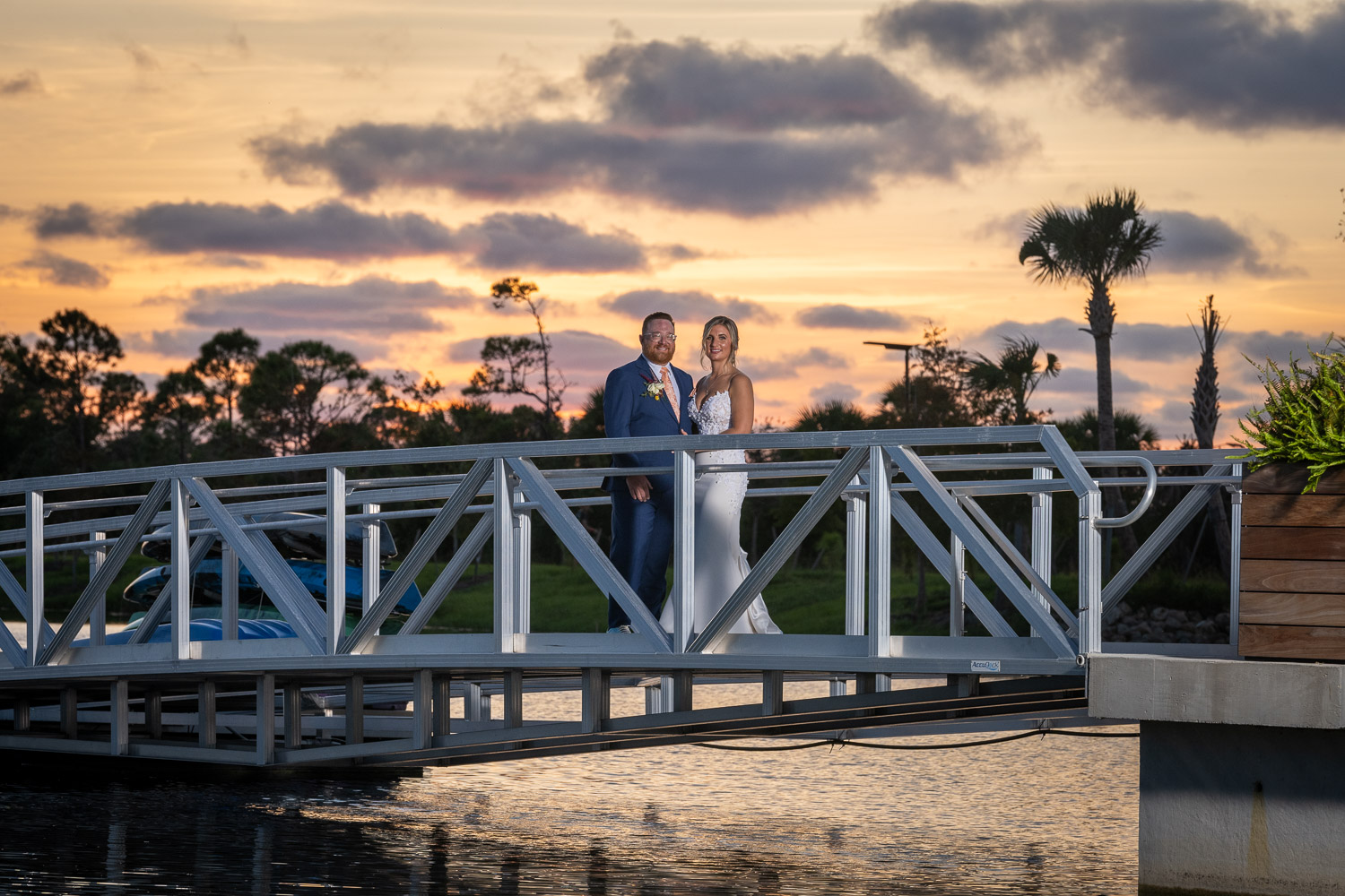bride and groom stand on dock in Wellen Park as the sun sets behind them