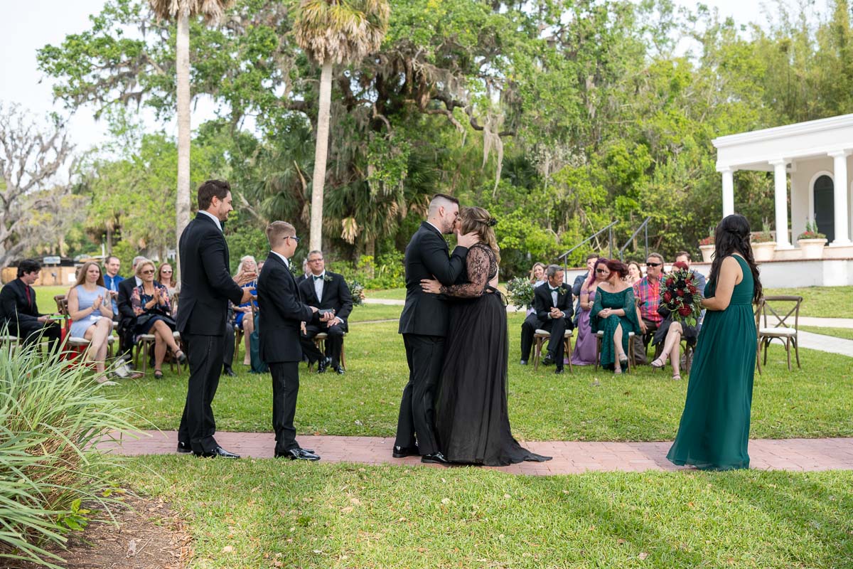 the bride and groom kiss with the guests looking on in the background