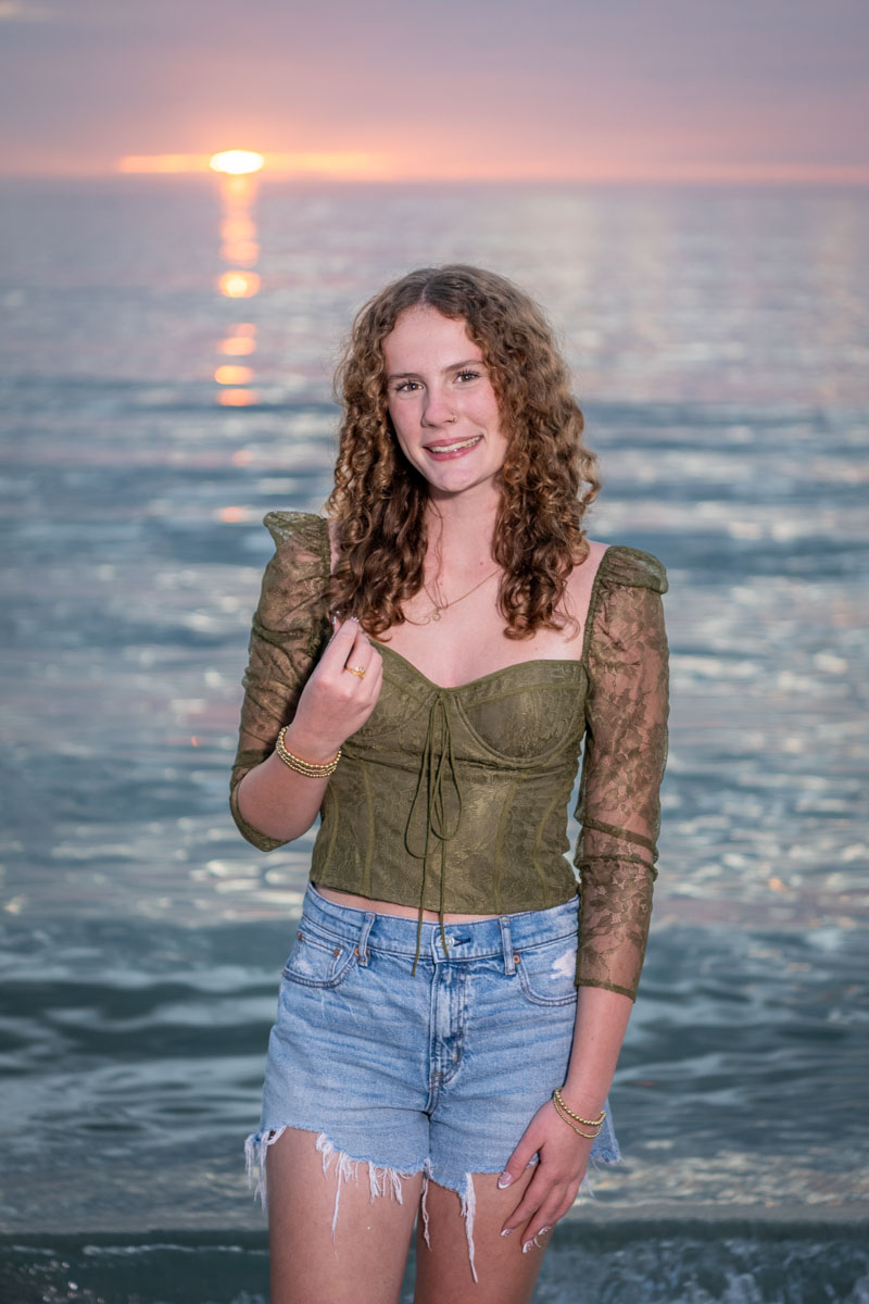 senior plays with her long hair with the sunset behind her