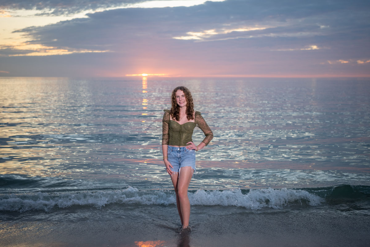 senior session on the beach with girl smiling as the sunsets behind her