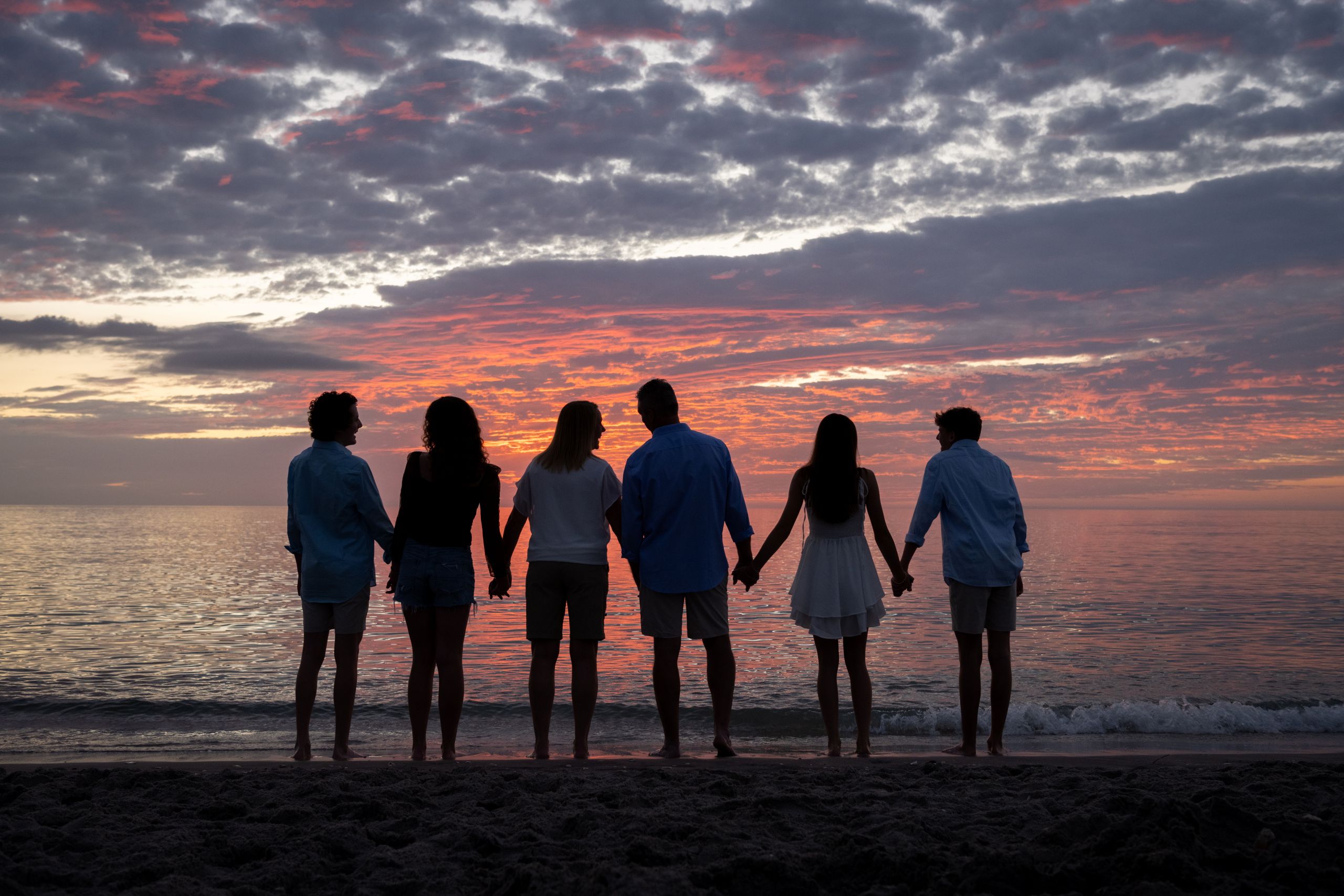 silhouette of family as they hold hands on the beach as the sun sets