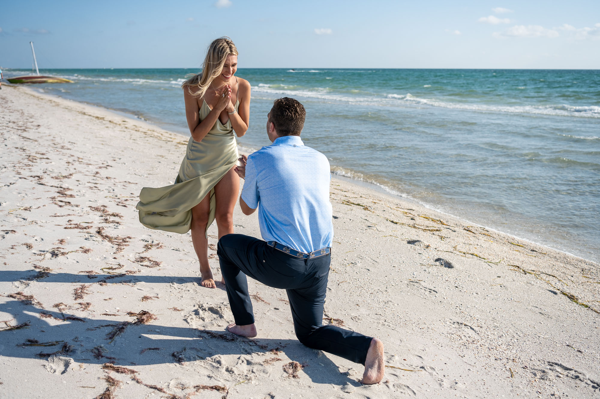 man surprises his girlfriend on the beach by dropping to his knee to propose