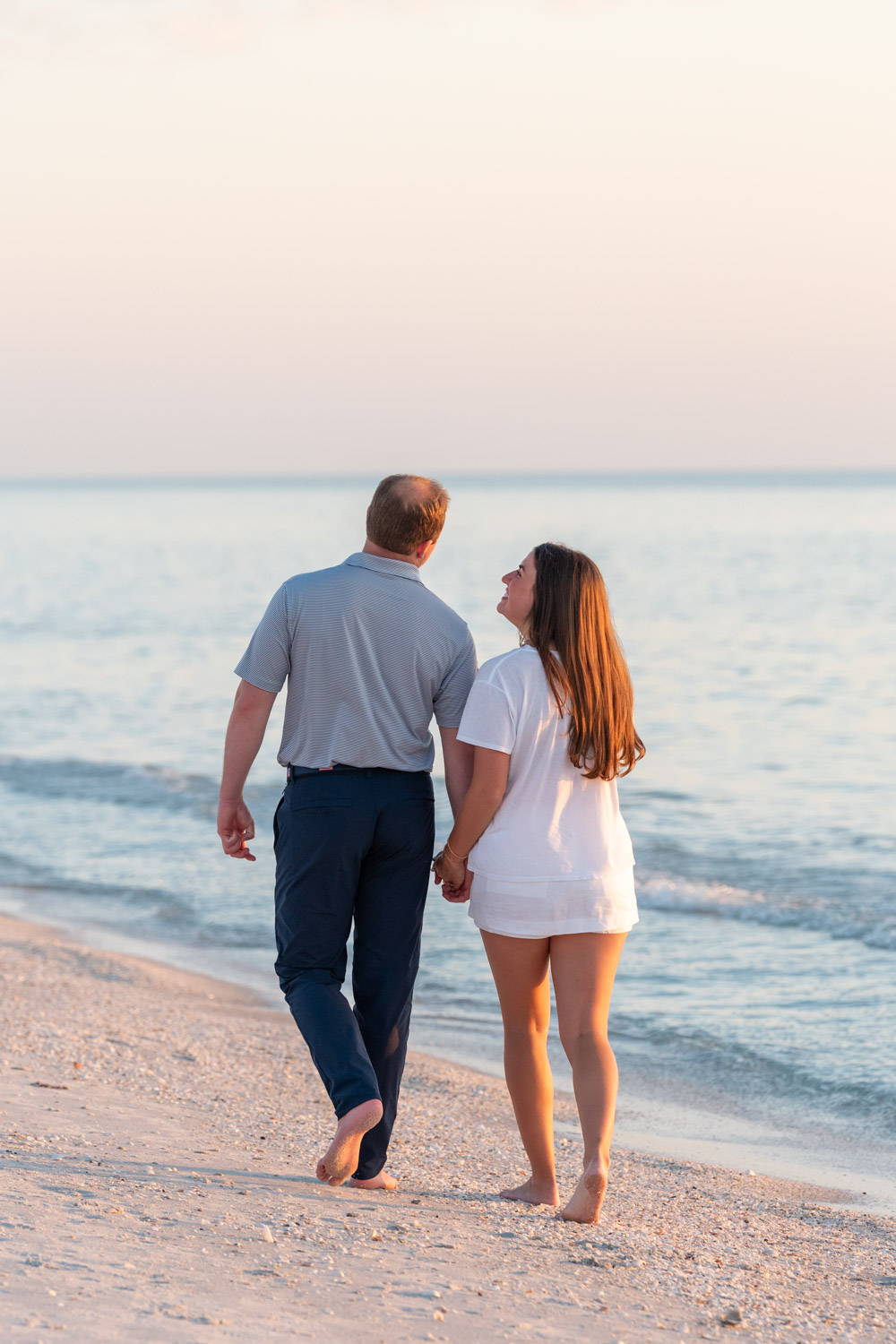 couple walk along the beach as they smile at each other