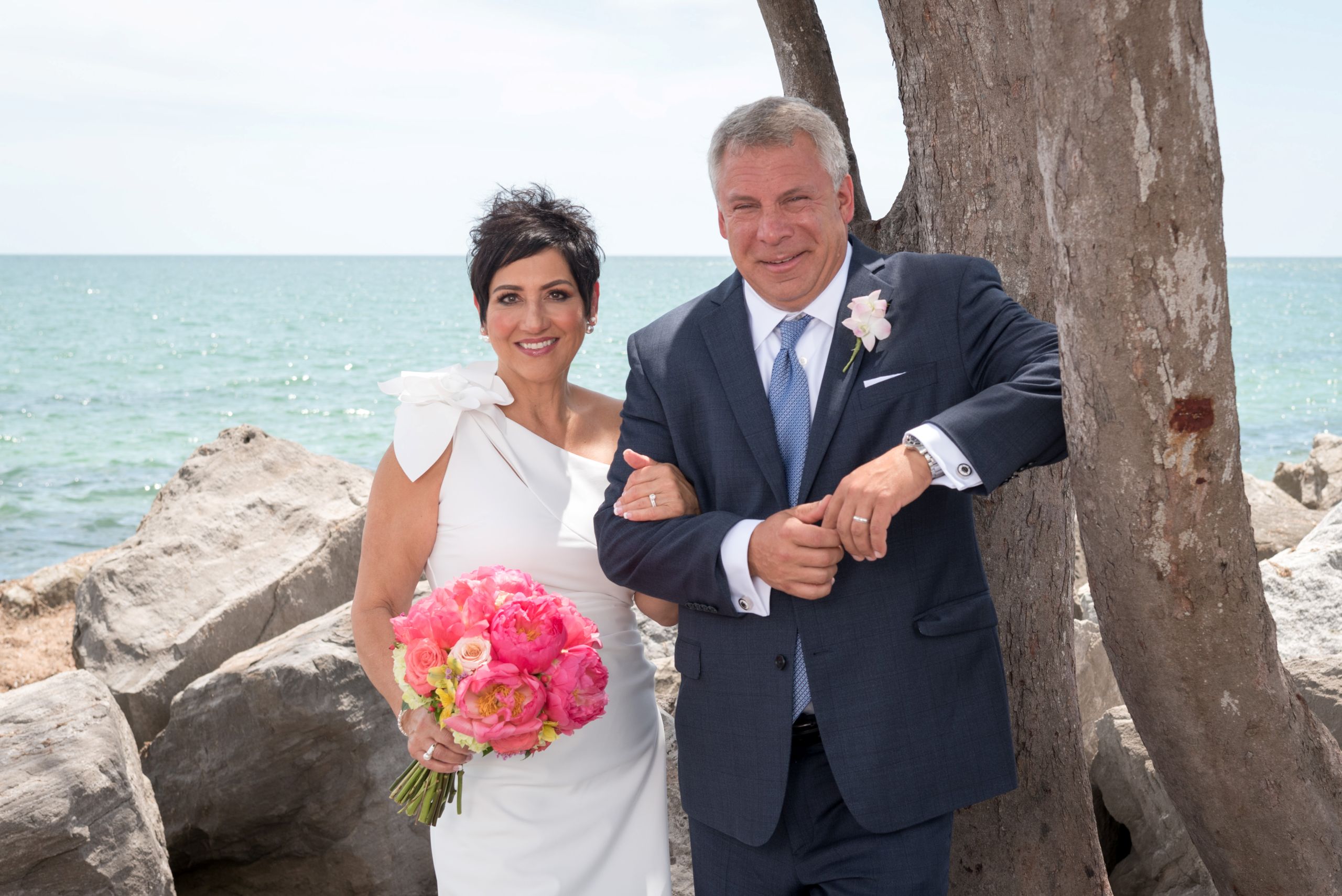 bride and groom smile as they stand by a tree