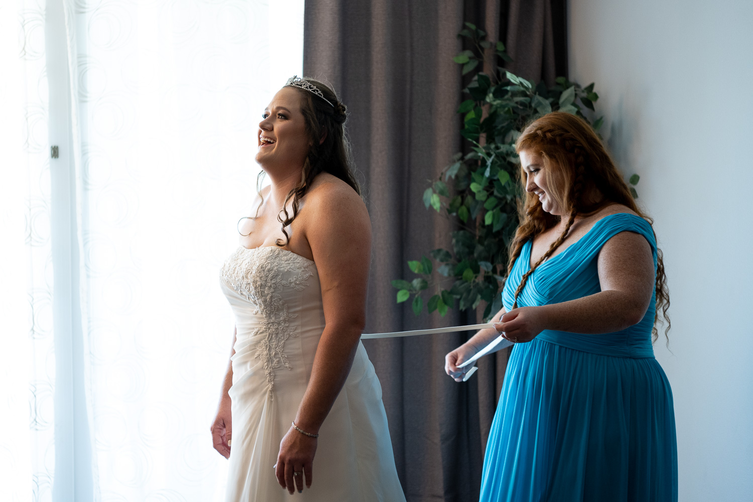 bridesmaid help bride get into her wedding dress