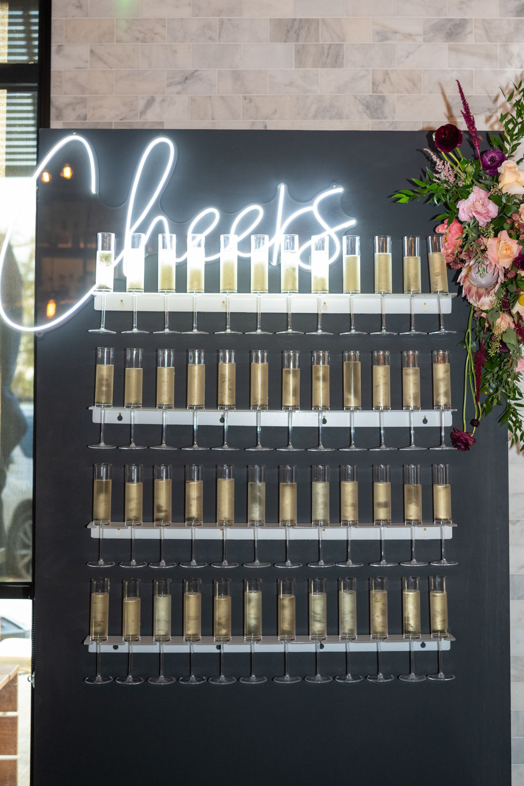 Champagne tower with "Cheers" in lights at wedding reception