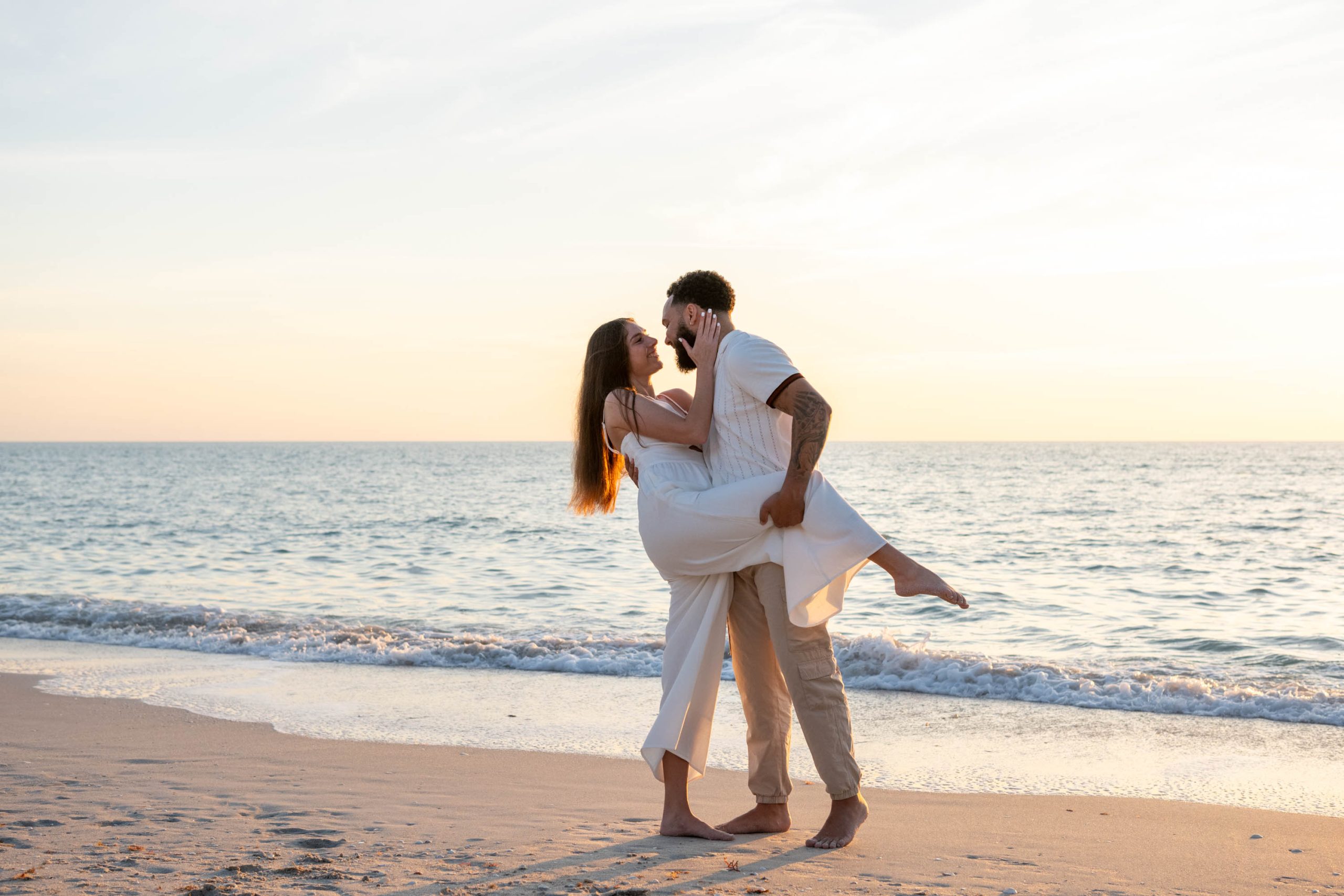 girl lifts her leg up and her fiance holds it as they embrace on the beach