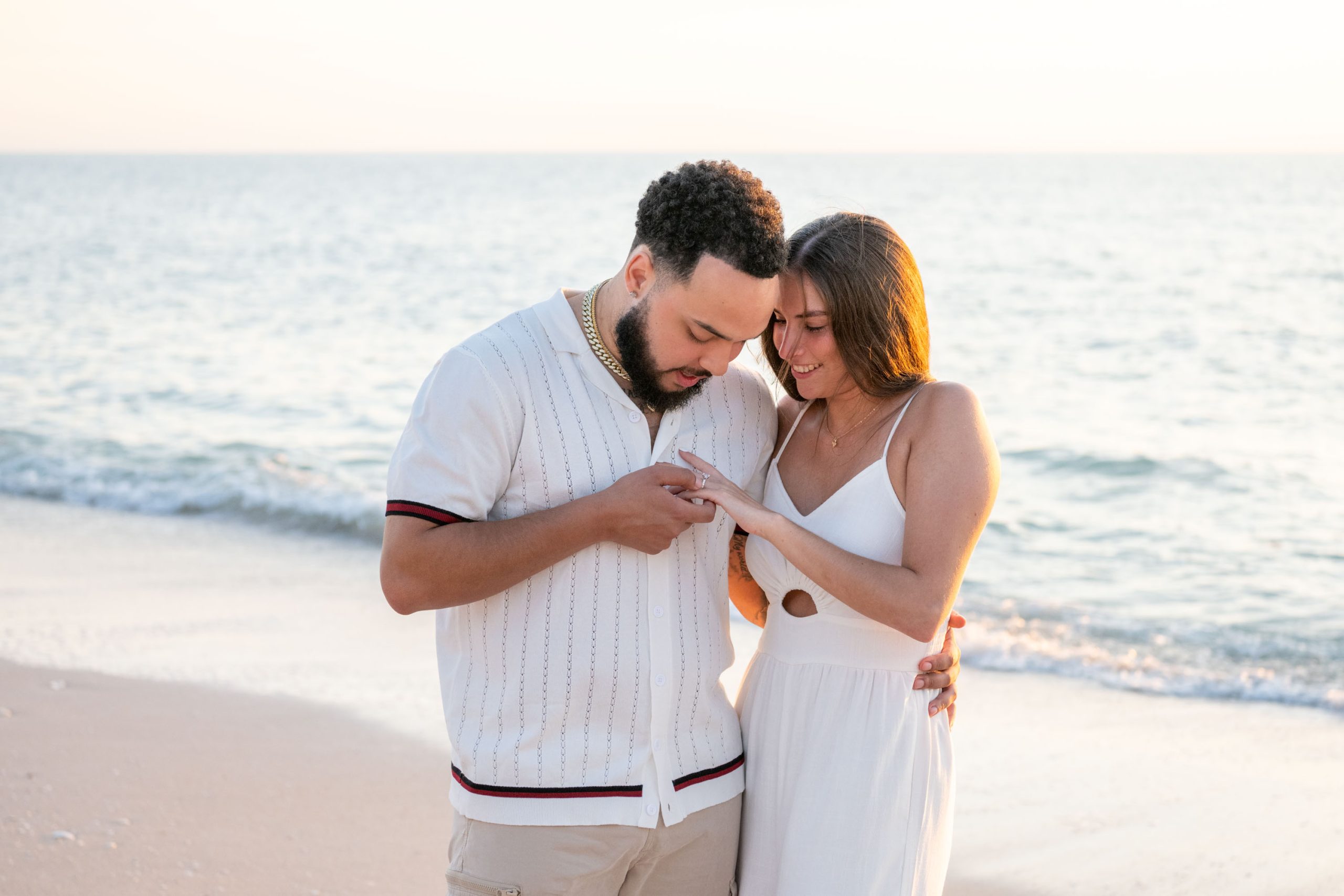 newly engaged couple look at her ring as the calm Gulf water is seen in the background