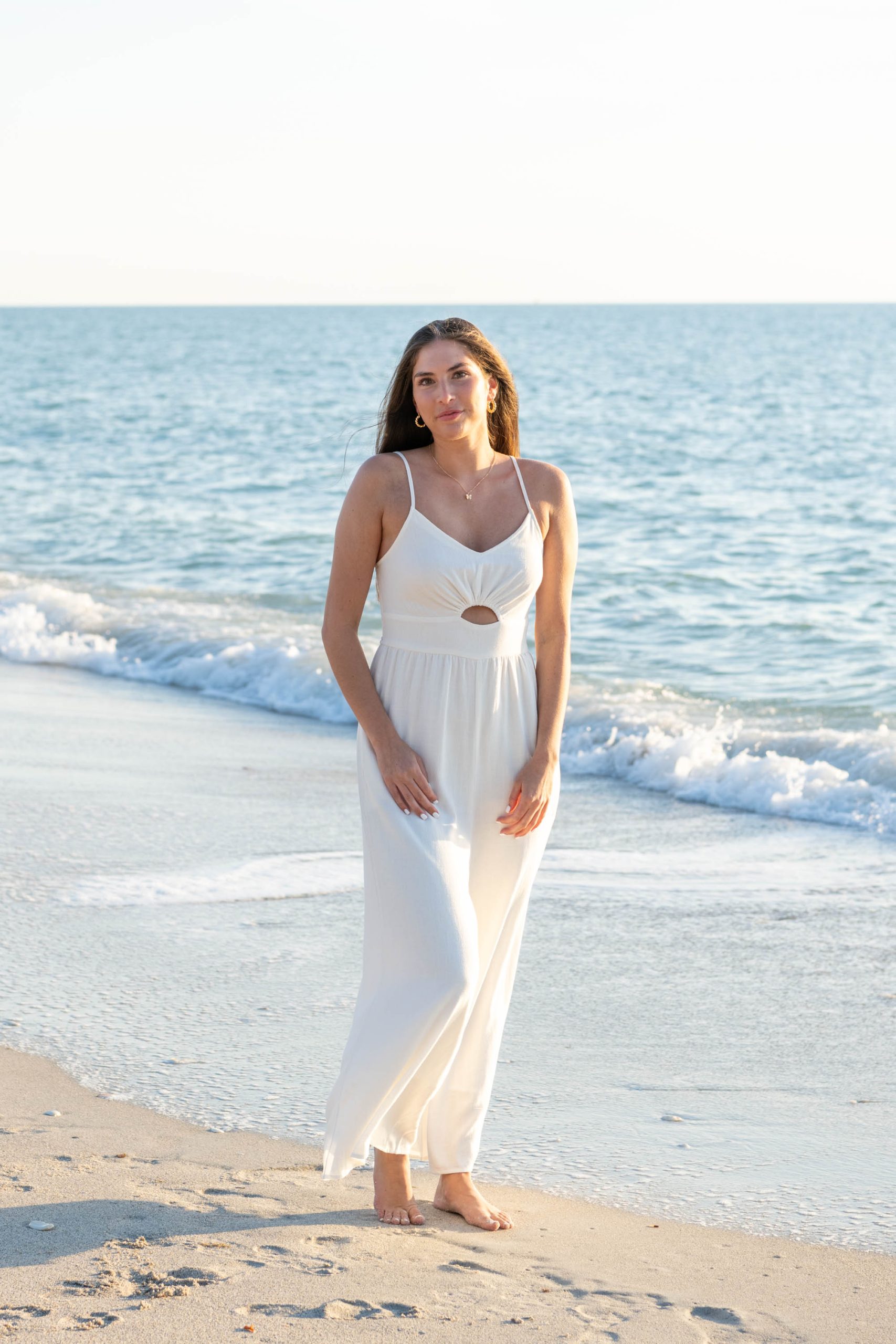 girl in white dress on the beach with the blue Gulf water rolling in behind her