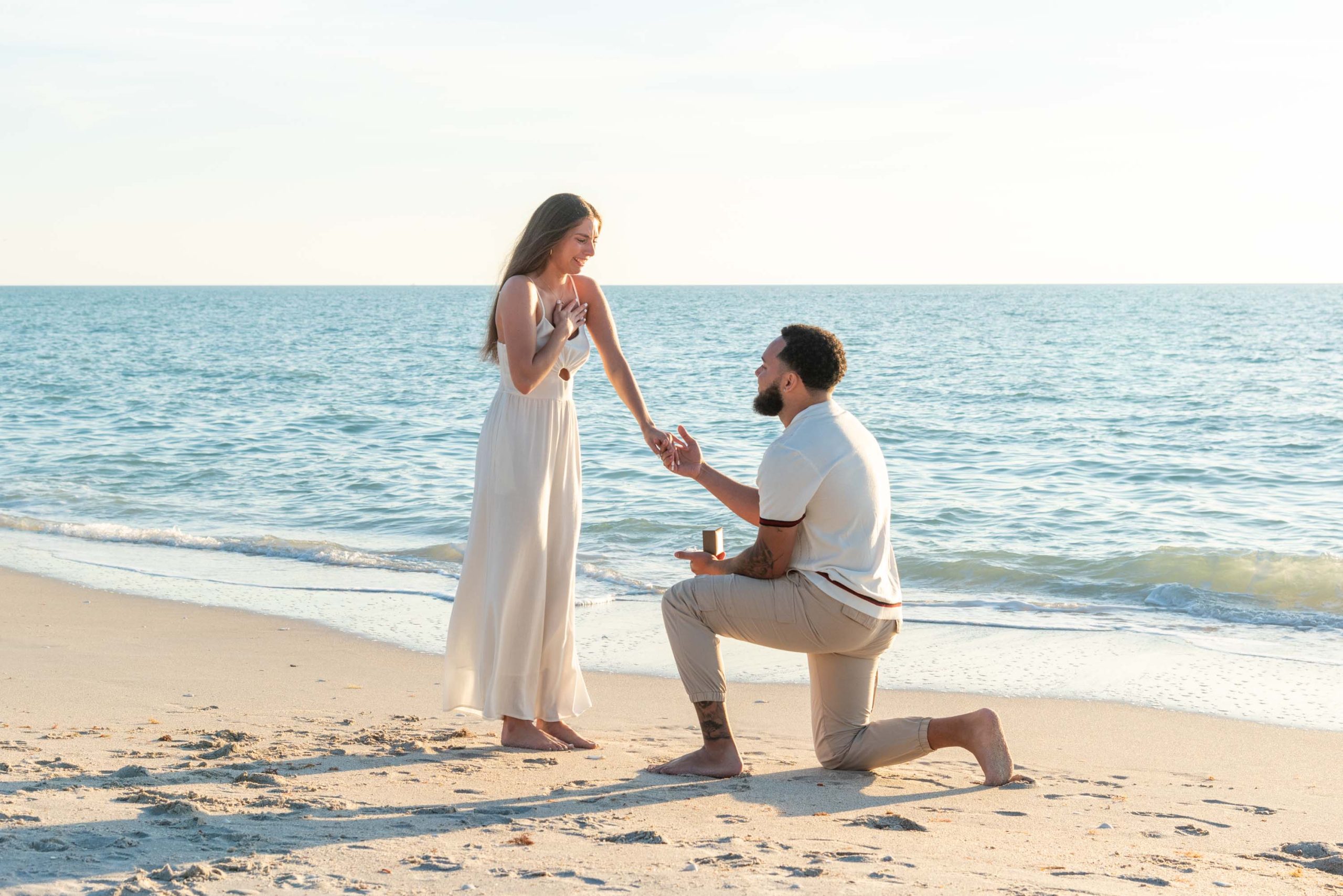 man drops down on his knee to propose to his girlfriend on the beach 