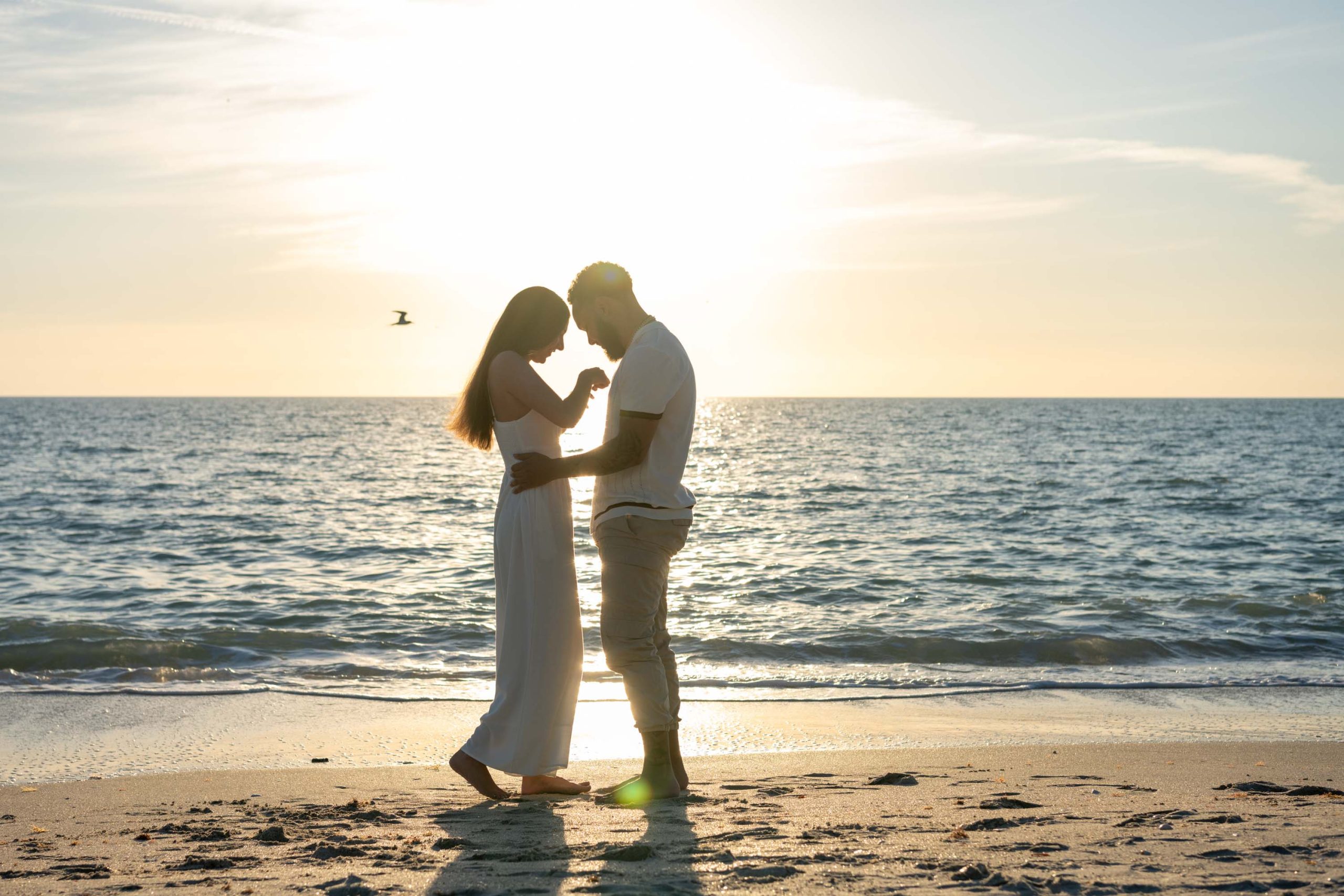 silhouette of couple on Casey Key beach as they face each other and look down at the engagement ring on her finger