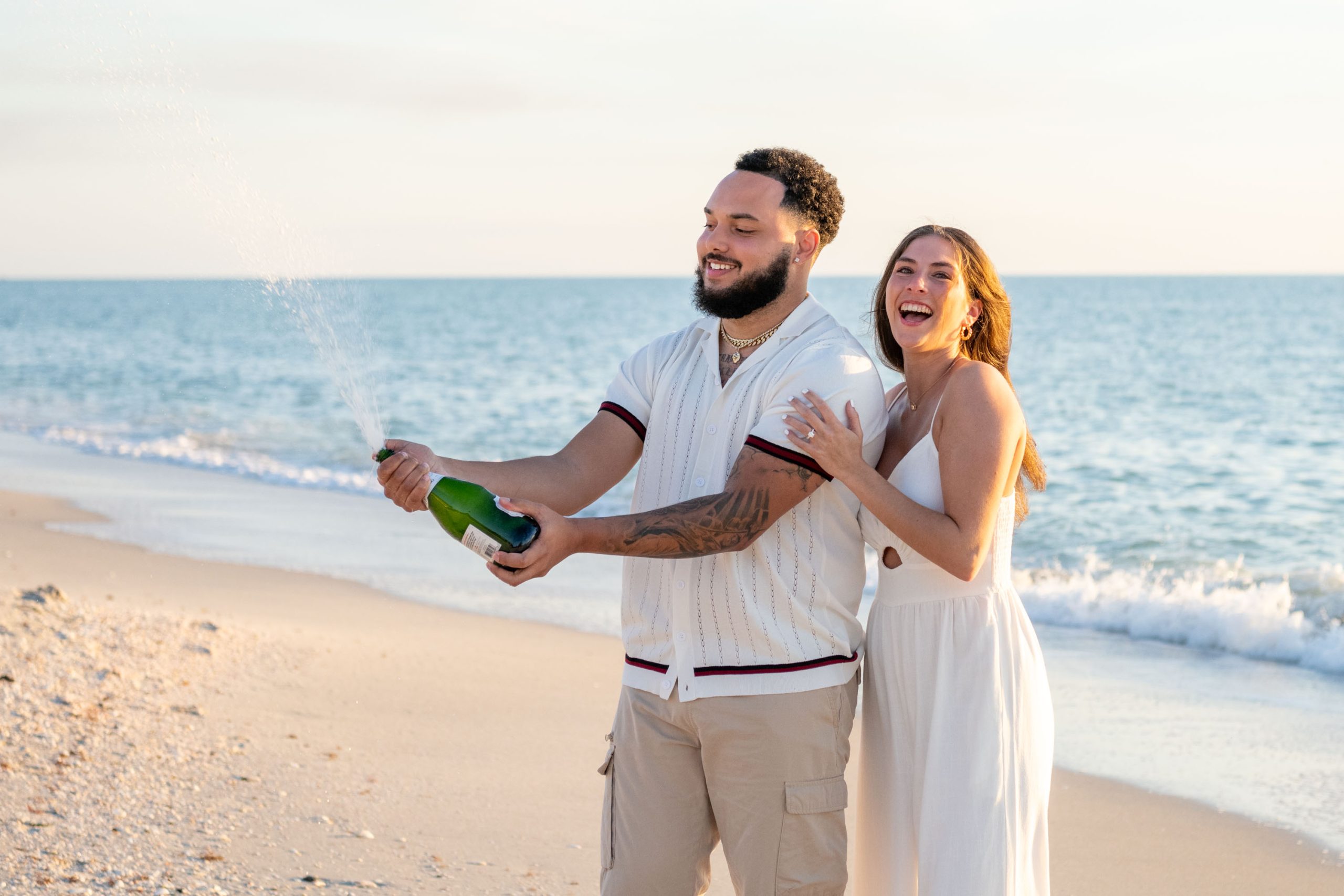 after engagement on Casey Key beach, couple celebrate by opening and spraying a bottle of champagne