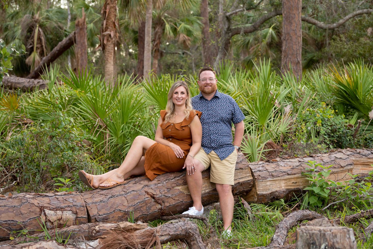 man and woman sit on log in woods looking relaxed and happy