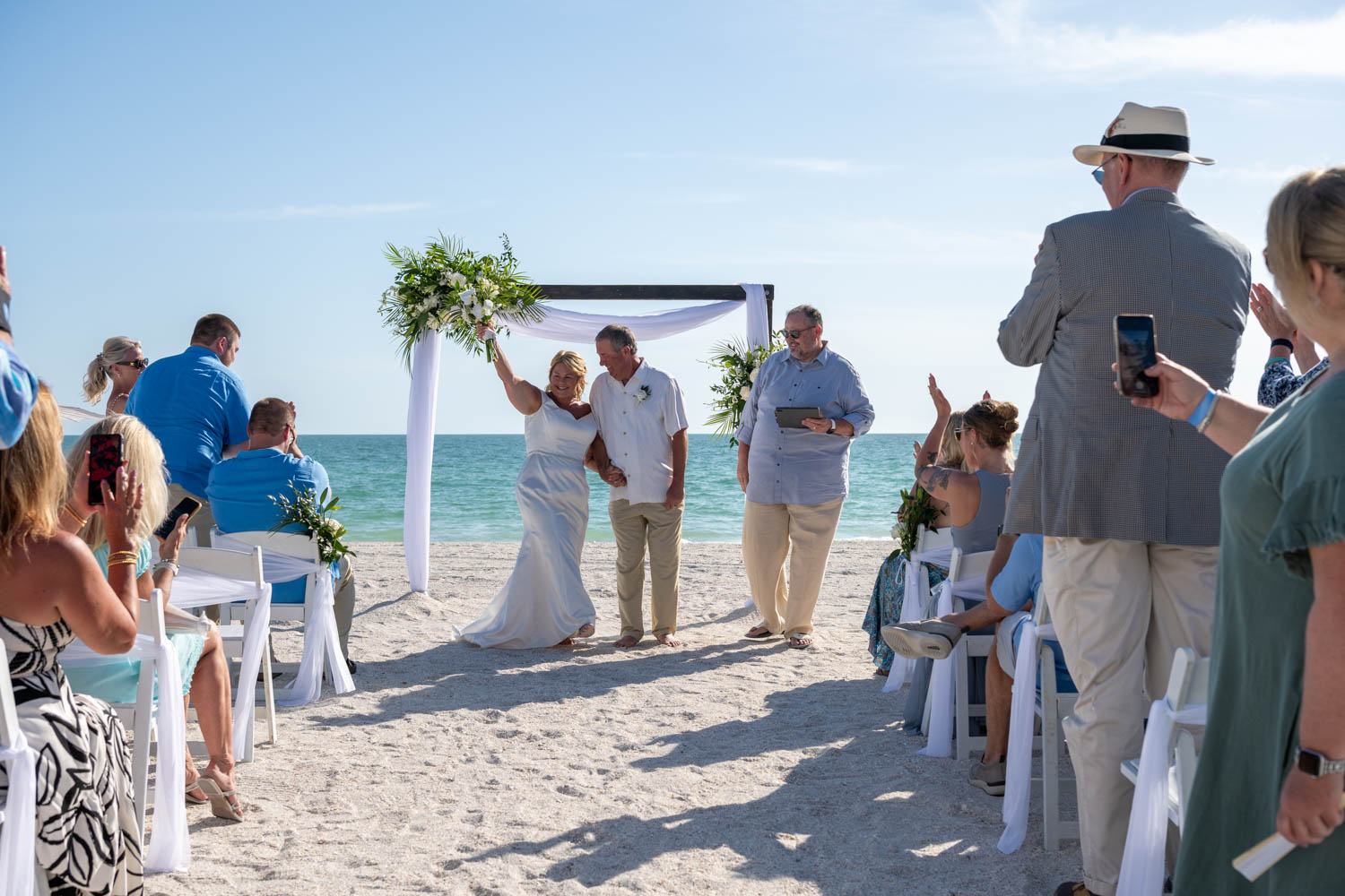 bride raises her arm and bouquet in celebration after wedding at Lido Beach Resort