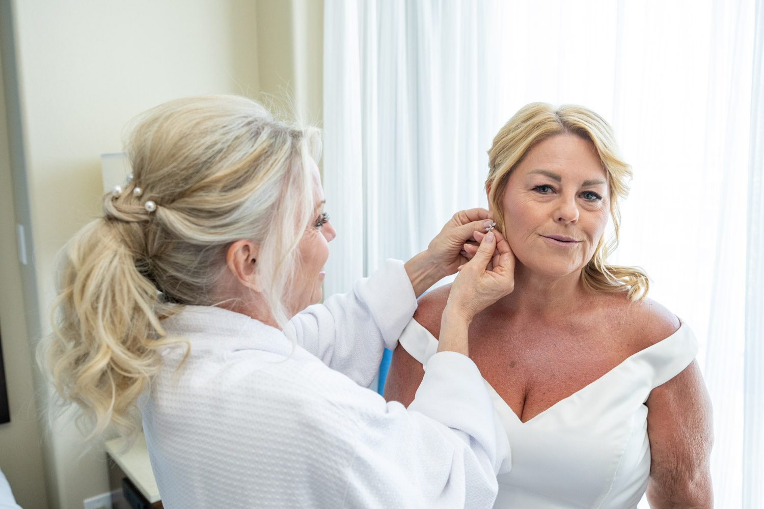 sister helping bride put on earrings