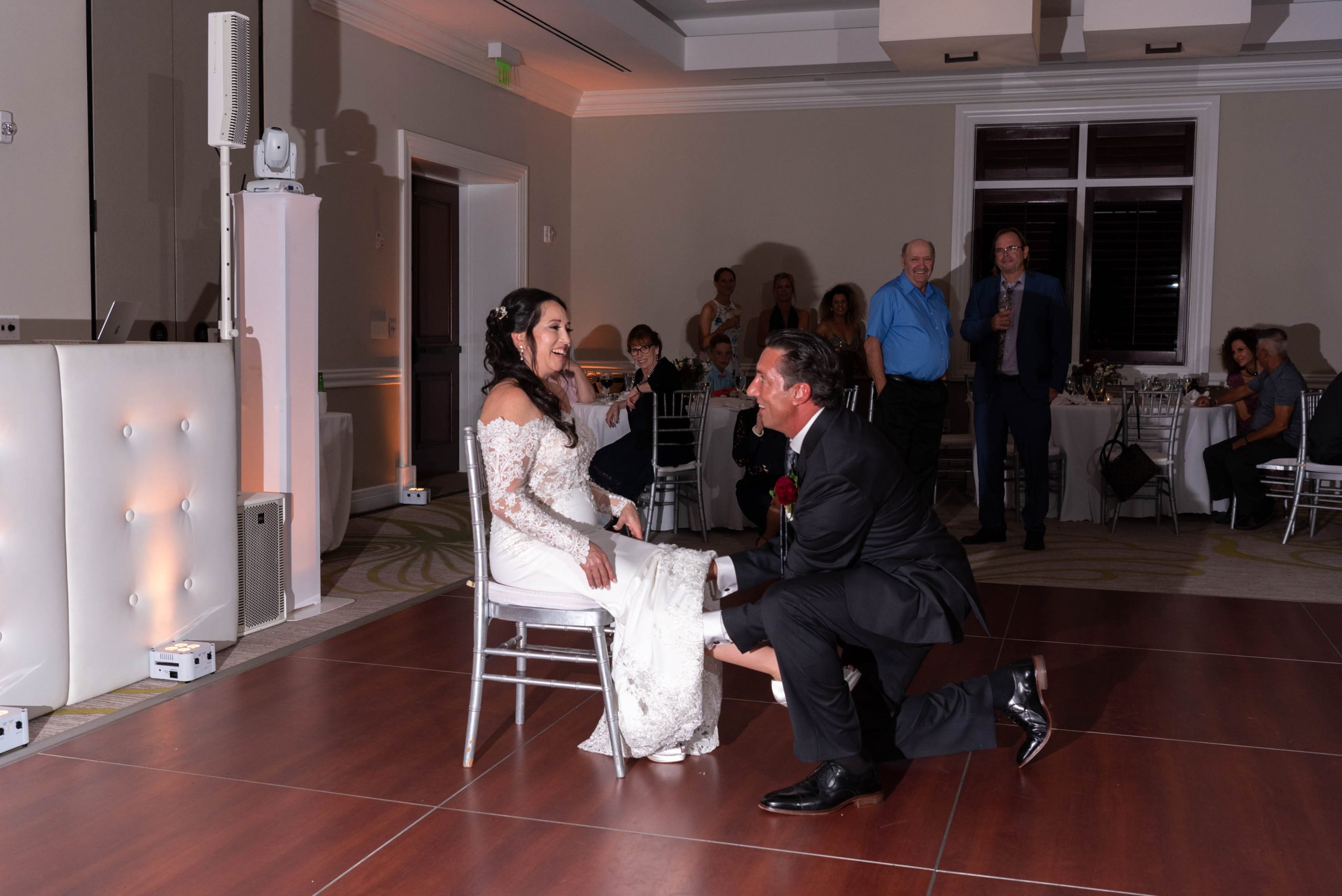 groom gets ready to remove garter from his wife as she sits in a chair
