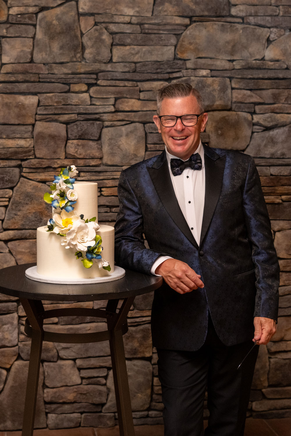 groom laughs as he stands by the wedding cake