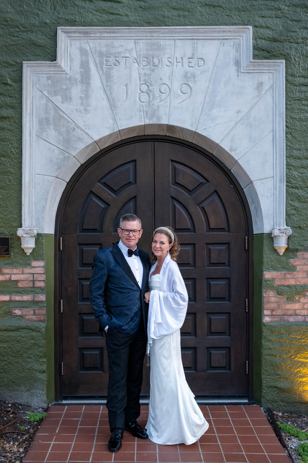 bride and groom stand in front of arched wood door at Sage SRQ after their wedding
