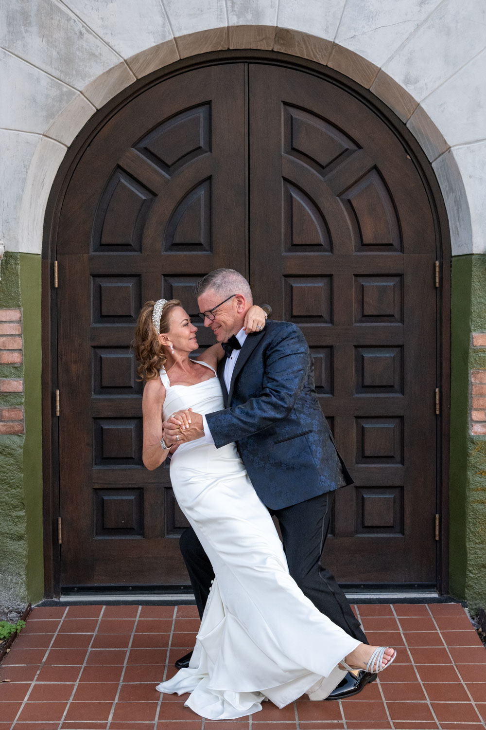 bride and groom smile as the look at each other as he dips her in front of an arched wood door at Sage SRQ